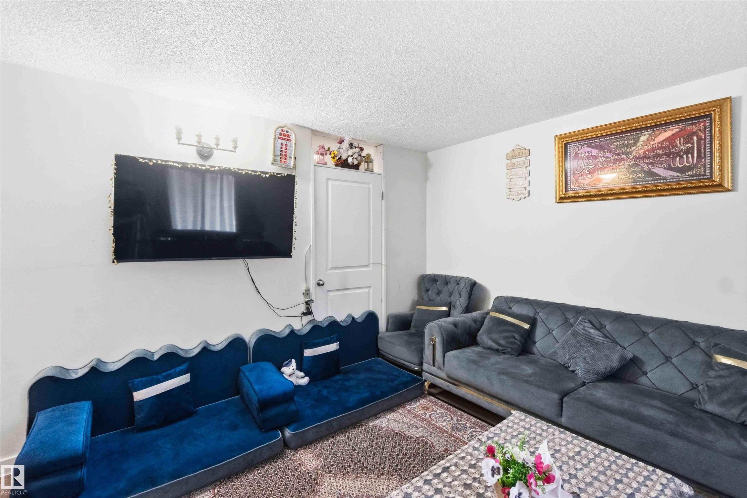 Living area featuring white walls, a textured ceiling, and a wall-mounted light fixture - 203 11421 34 Street Nw, Edmonton, AB