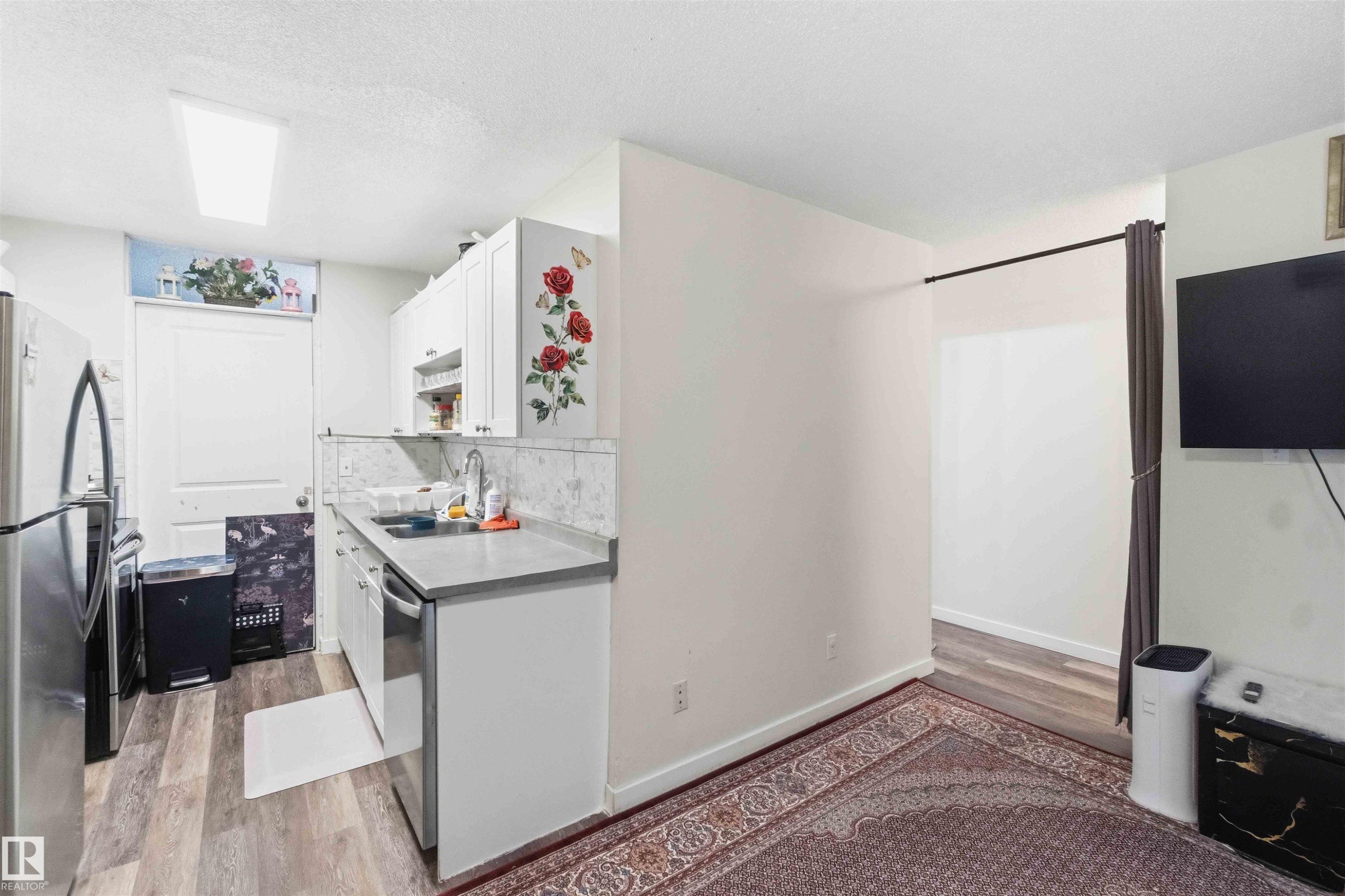 Compact kitchen featuring white cabinetry, a stainless steel dishwasher, and a grey countertop - 203 11421 34 Street Nw, Edmonton, AB