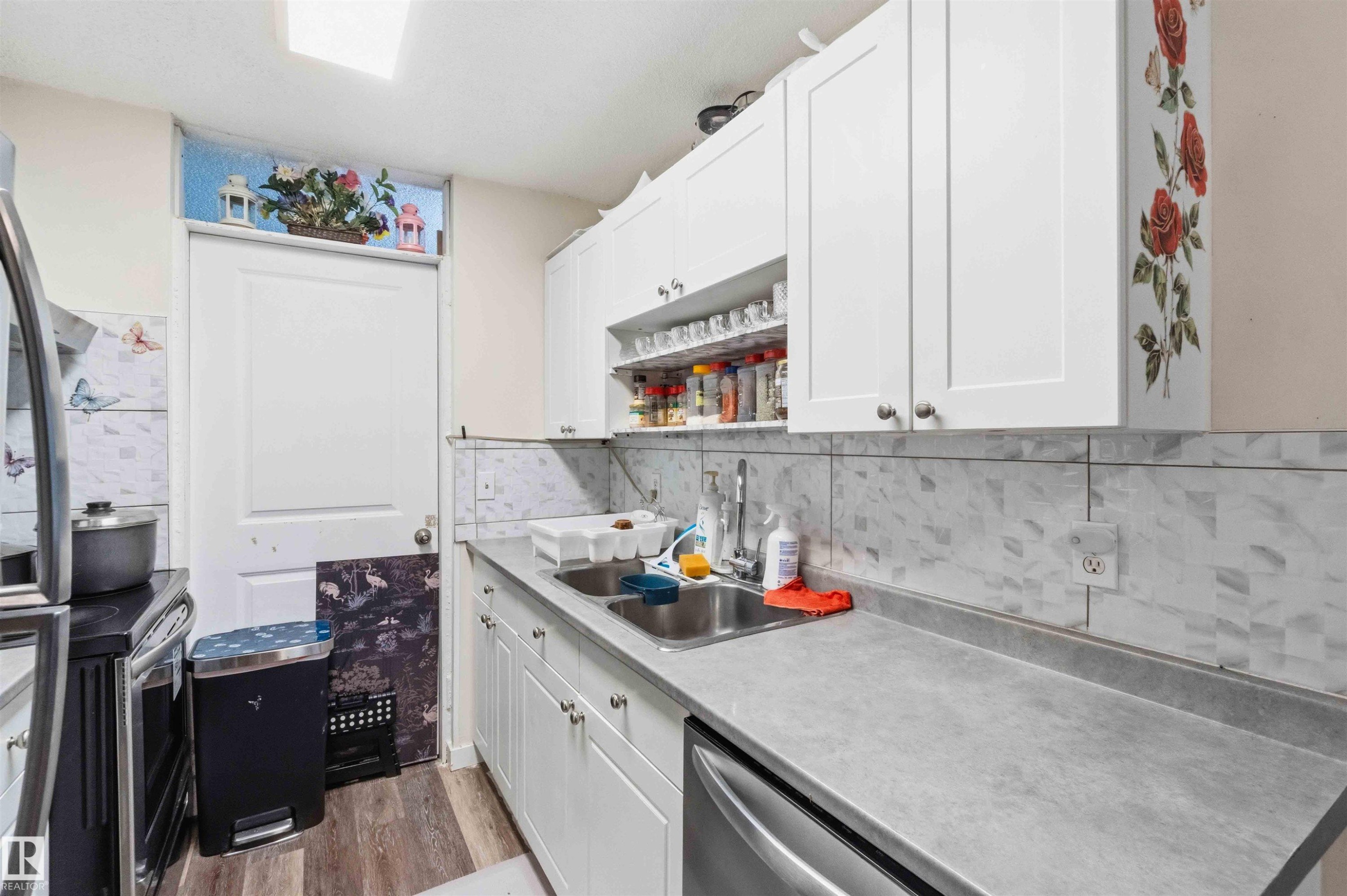 Kitchen featuring white shaker-style cabinetry, a double basin stainless steel sink, and a gray countertop - 203 11421 34 Street Nw, Edmonton, AB