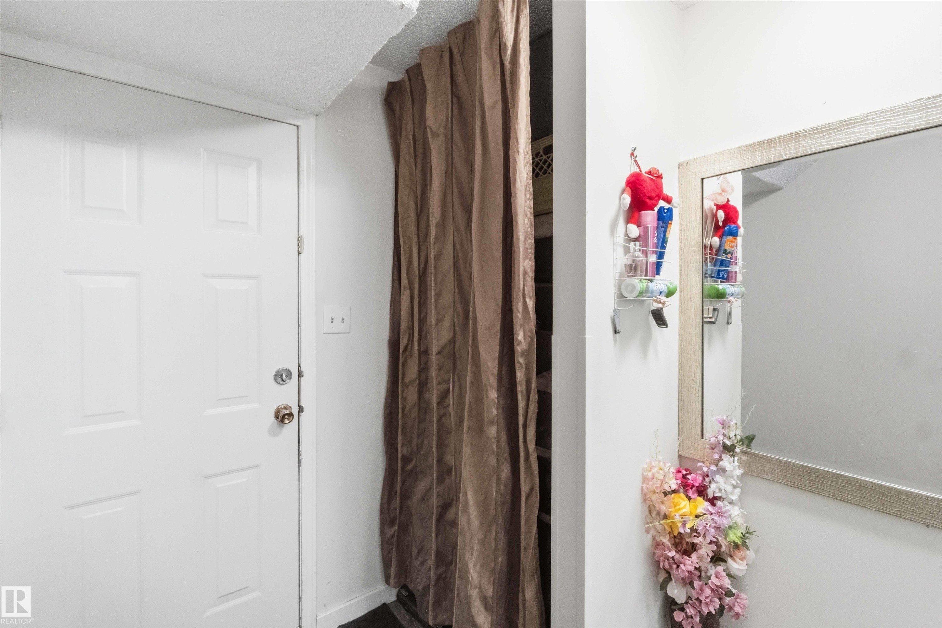 White paneled door with brass-toned hardware, complemented by a textured ceiling and a full-length mirror with a light-toned frame - 203 11421 34 Street Nw, Edmonton, AB