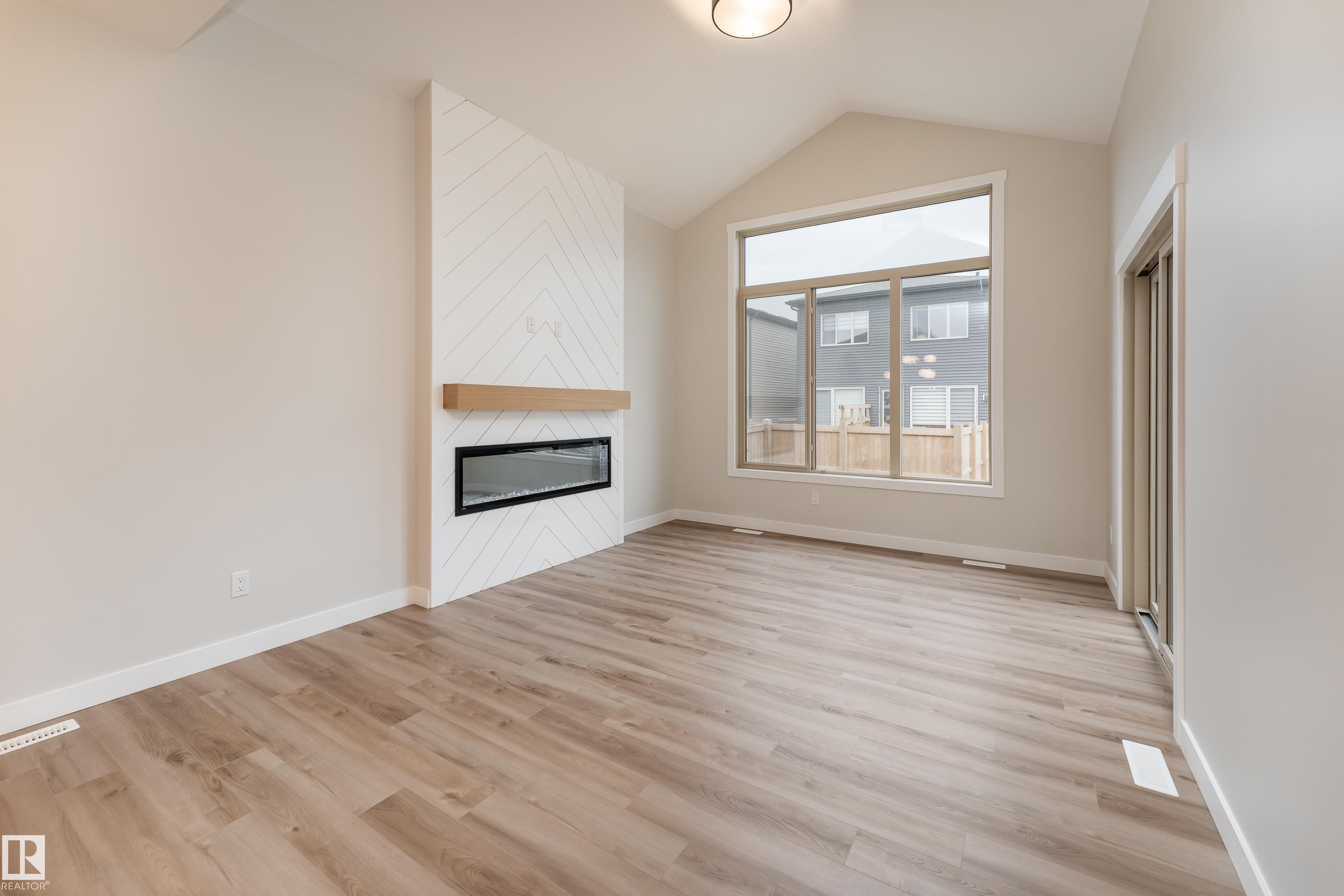 Contemporary living room featuring wood-finish flooring, a vaulted ceiling, and a fireplace with a chevron-patterned surround and a wood mantel - 115 Garneau Gate, Spruce Grove, AB