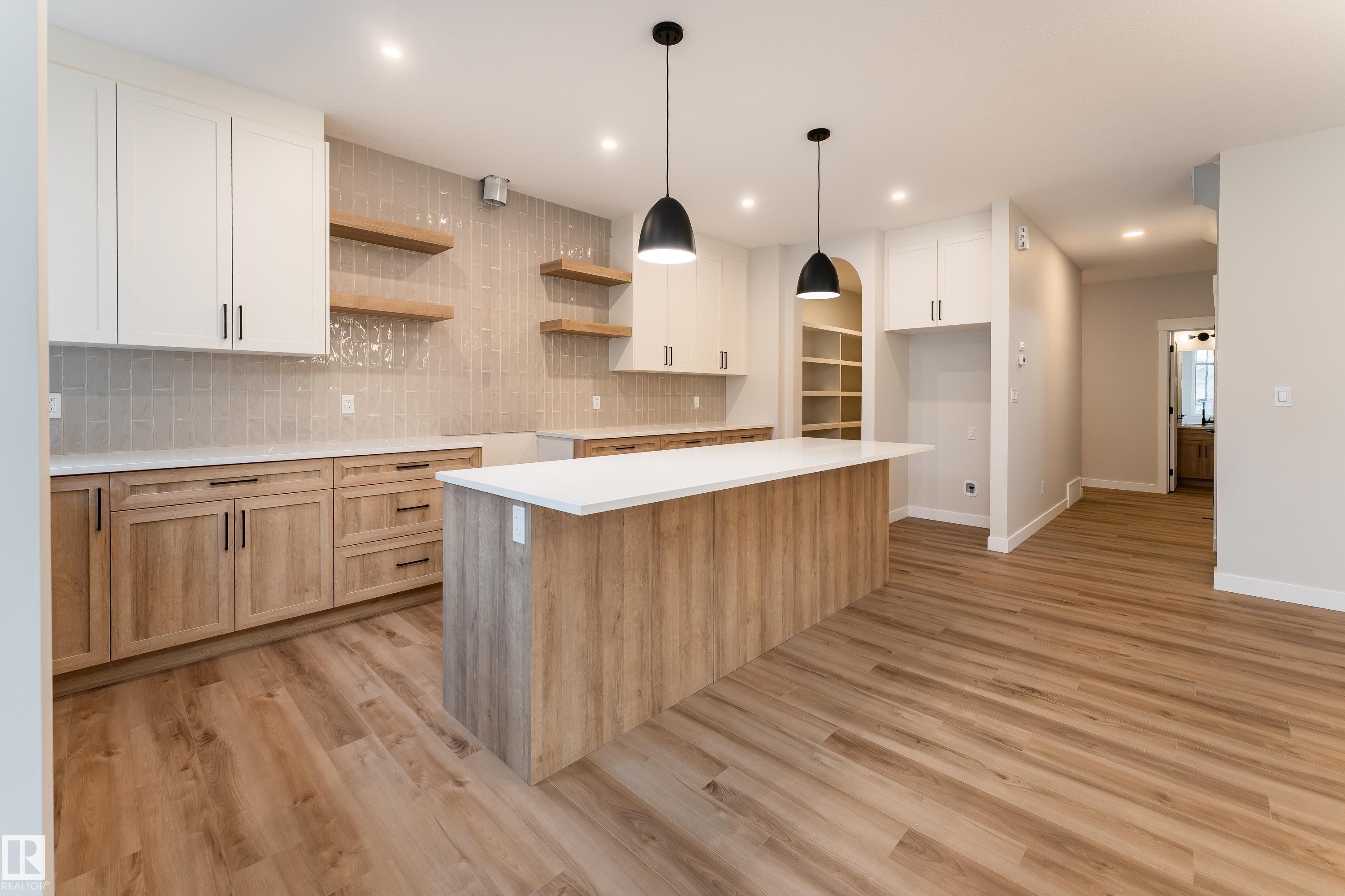 Modern kitchen featuring a large central island with a white countertop, two pendant lights, and wood-finish cabinetry - 115 Garneau Gate, Spruce Grove, AB