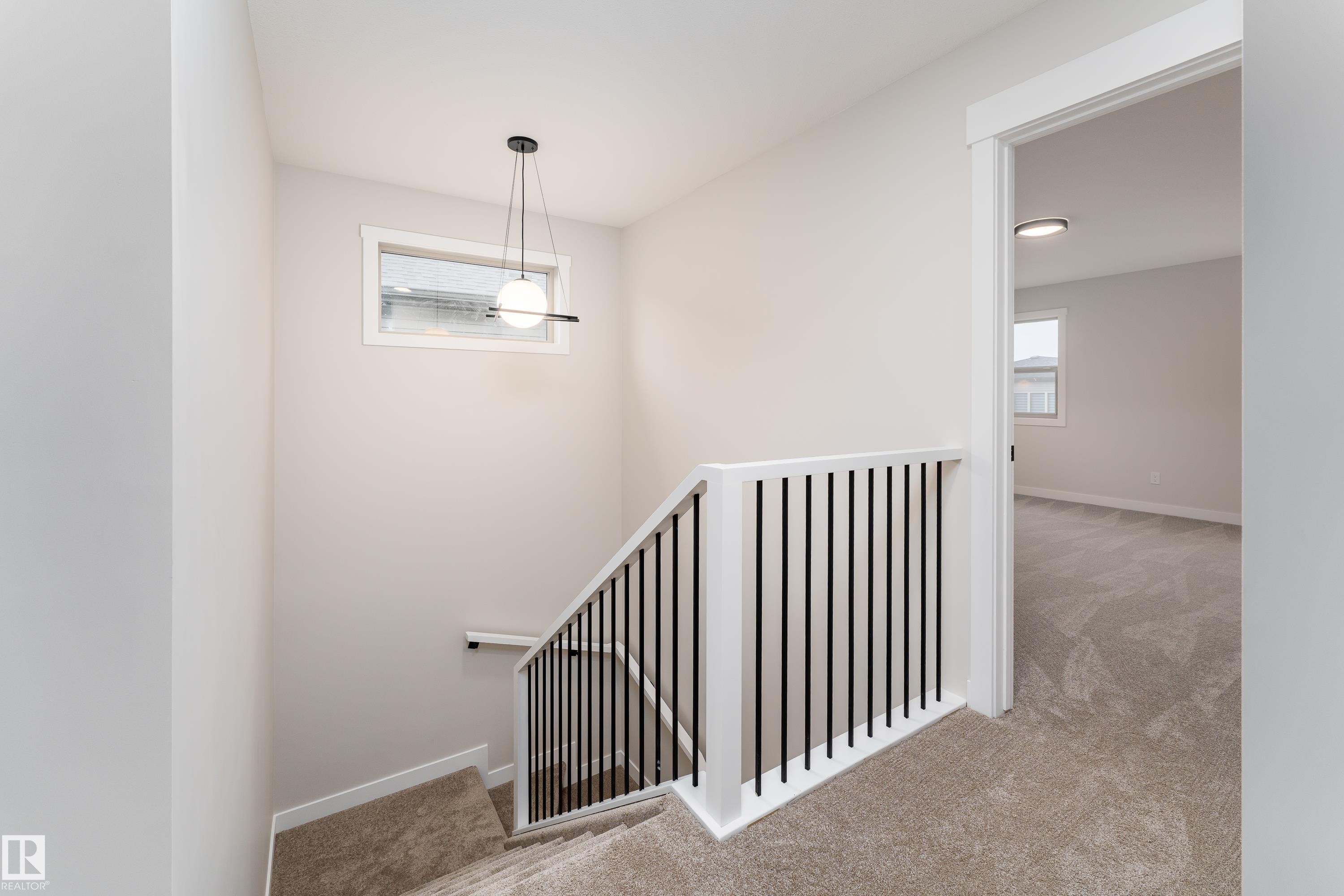 Staircase with modern black metal balusters, white handrail, and carpeted treads - 115 Garneau Gate, Spruce Grove, AB