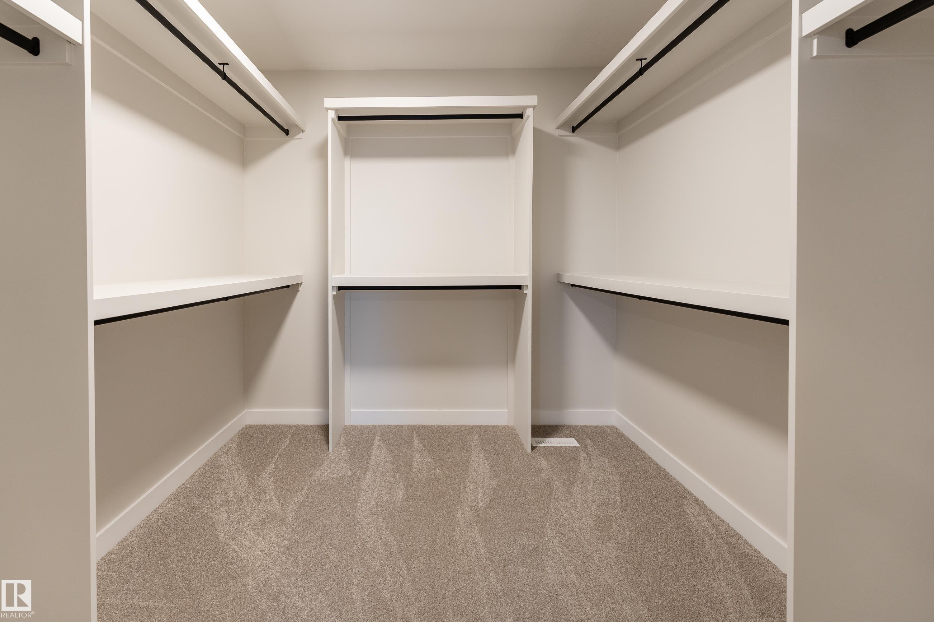 Walk-in closet featuring white built-in shelving, multiple hanging rods, and light-toned carpeting - 115 Garneau Gate, Spruce Grove, AB