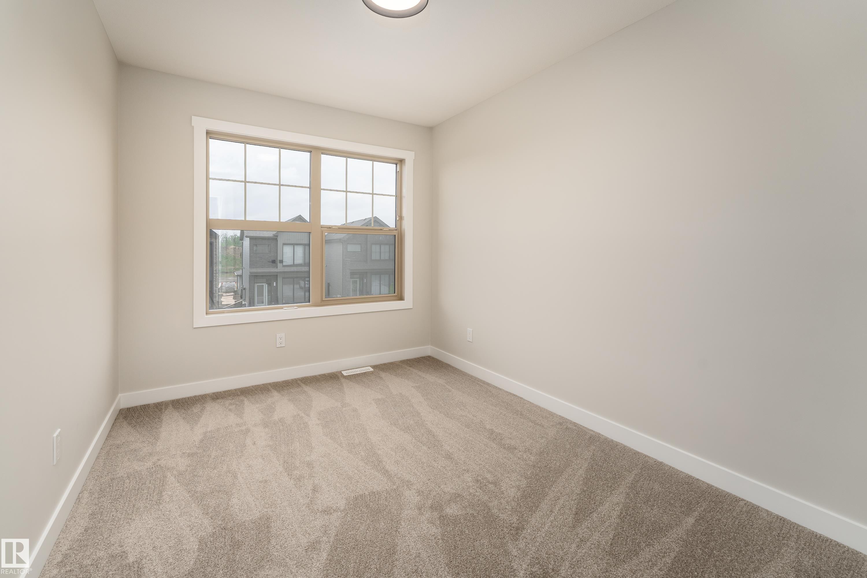 Neutral-toned room featuring a large window with white trim, light beige walls, and patterned carpeting - 115 Garneau Gate, Spruce Grove, AB