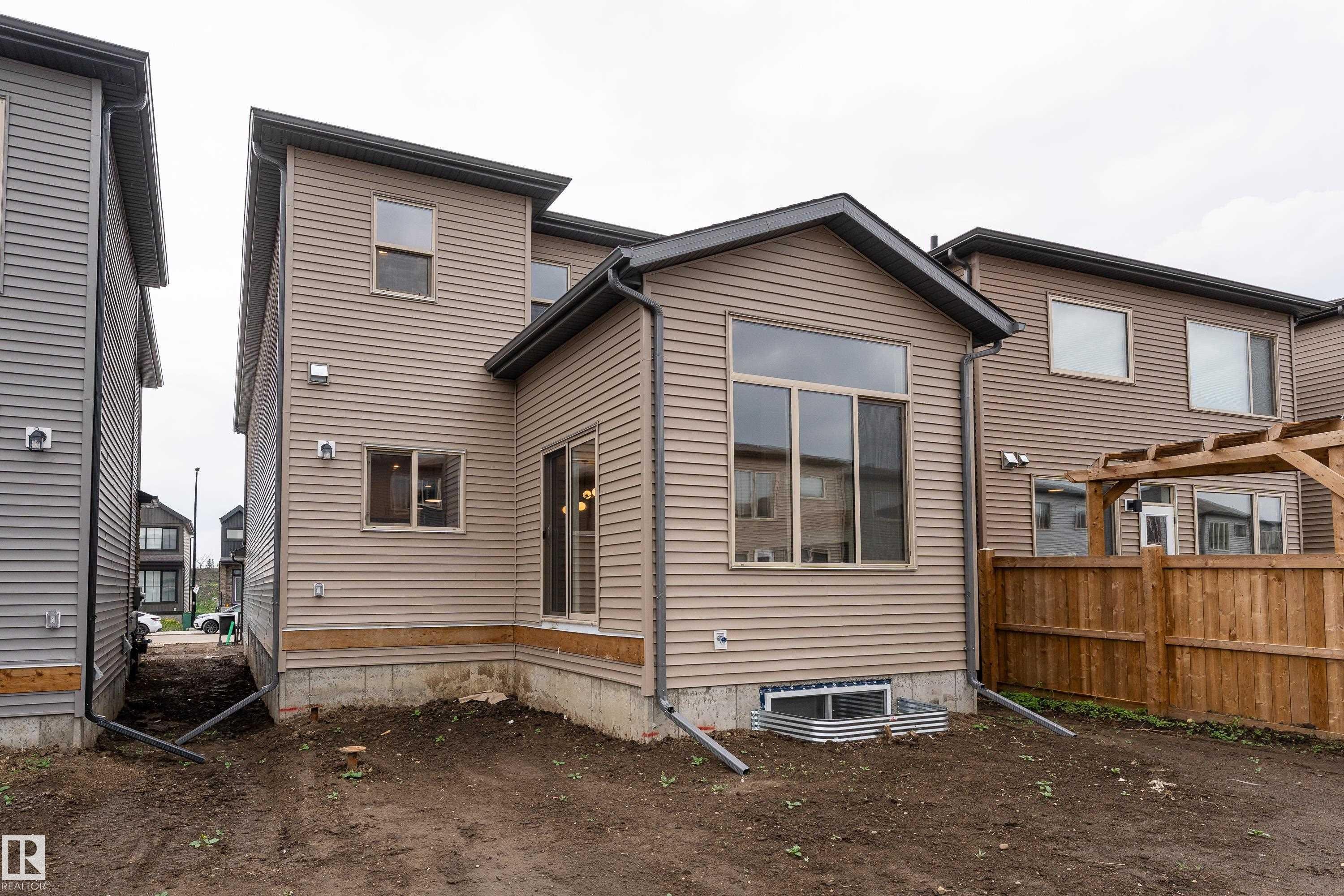 Rear exterior featuring horizontal siding, a large picture window, and an attached wood pergola - 115 Garneau Gate, Spruce Grove, AB