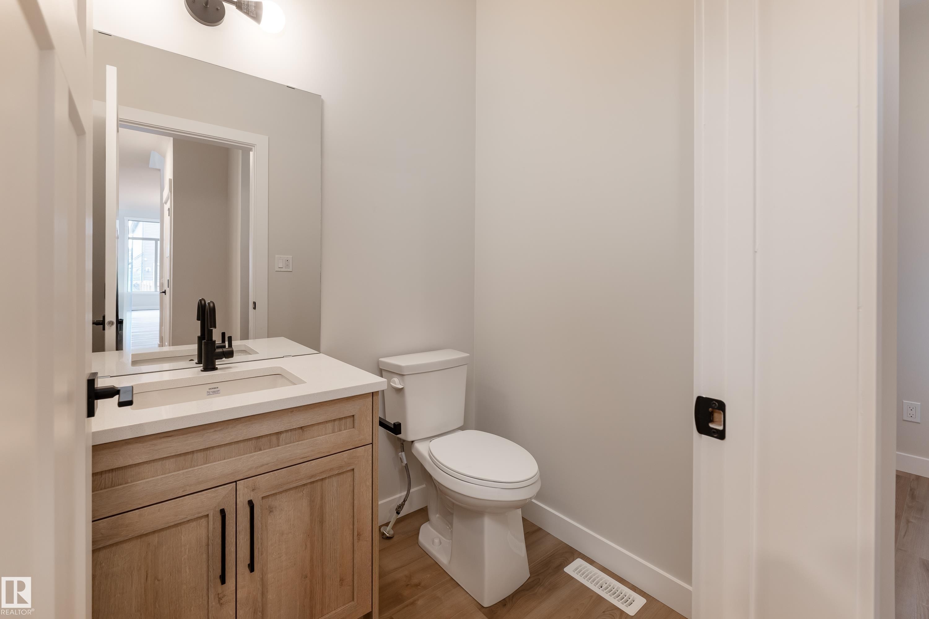 Powder room featuring a wood-finish vanity with a built-in rectangular sink, light-toned countertop, and matte black fixtures - 115 Garneau Gate, Spruce Grove, AB
