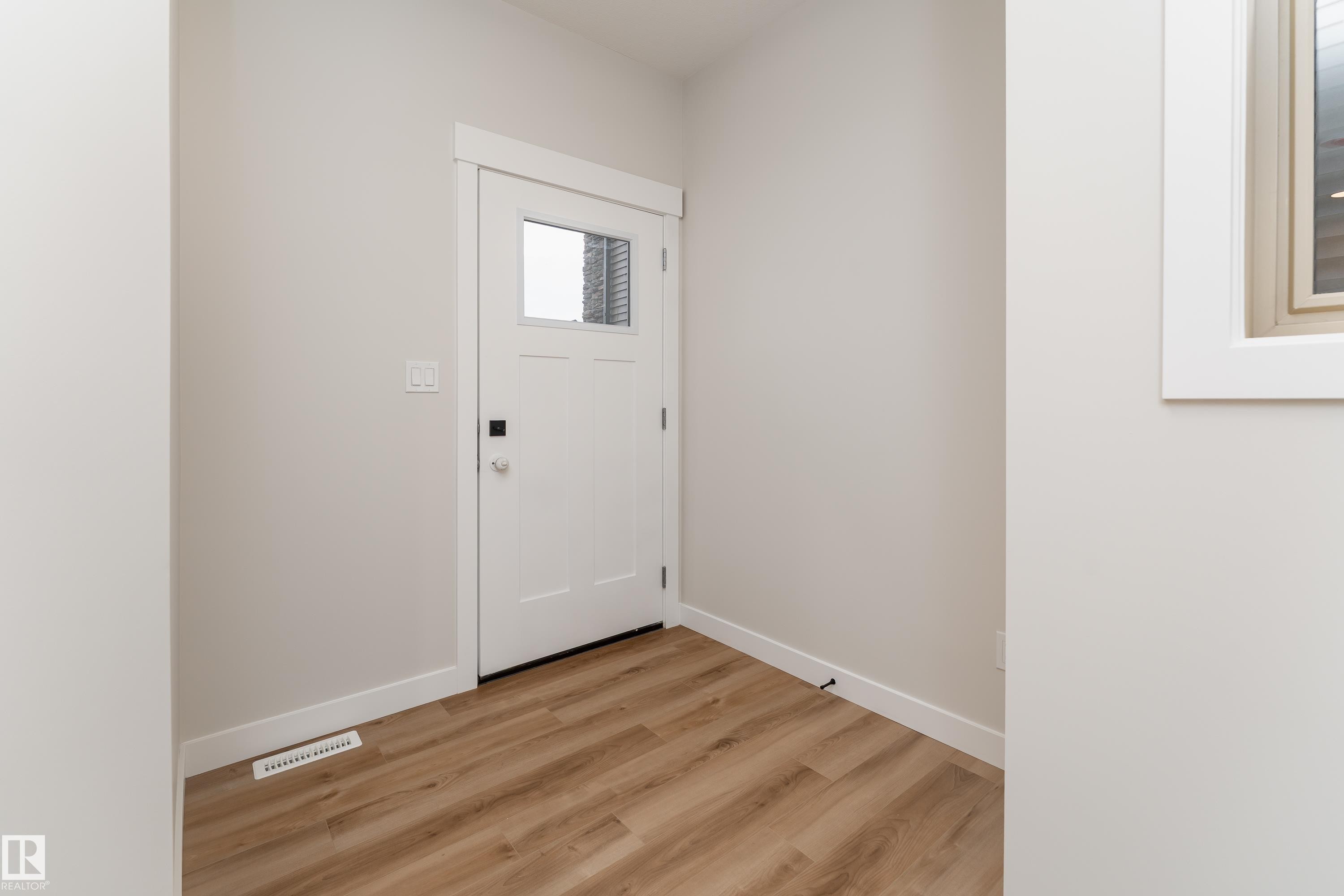 Entryway featuring a white paneled door with a clear glass insert, light wood-finish flooring, white baseboards, and neutral wall tones - 115 Garneau Gate, Spruce Grove, AB