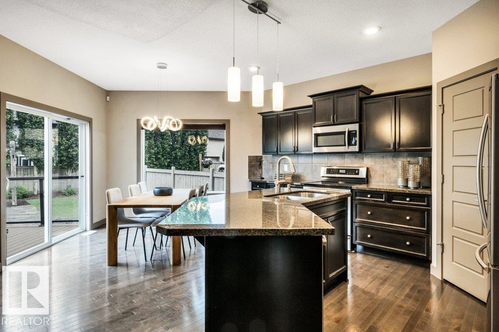 Kitchen featuring dark wood cabinetry, stainless steel appliances, a granite island with an undermount sink, and wood-finish flooring - 1107 Chahley Crest, Edmonton, AB