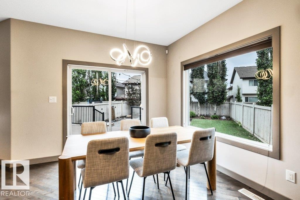 Spacious dining area featuring a contemporary chandelier, large picture window, and sliding glass door - 1107 Chahley Crest, Edmonton, AB