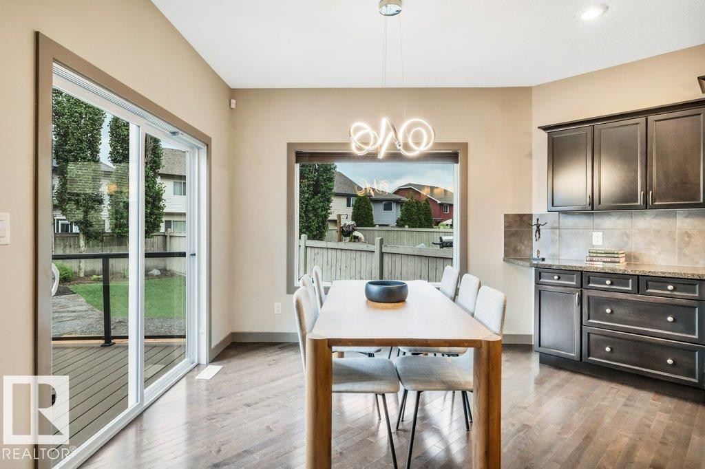 Dining area featuring wood-finish flooring, a contemporary chandelier, and a large window - 1107 Chahley Crest, Edmonton, AB