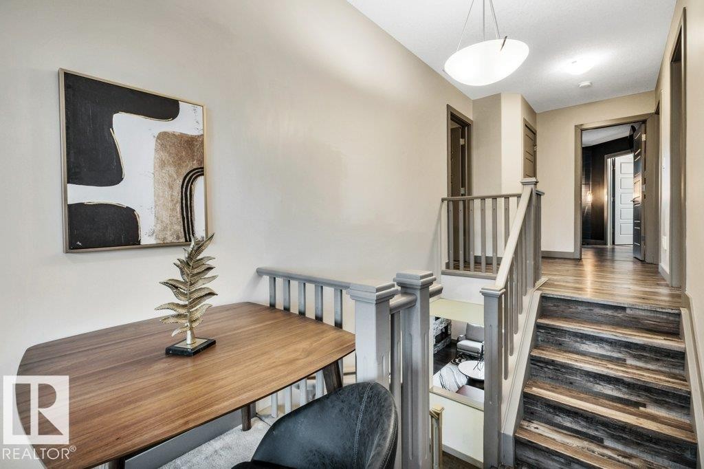 Upper-level landing featuring wood-finish flooring, a contemporary ceiling light fixture, and a staircase with a gray-painted railing and balusters - 1107 Chahley Crest, Edmonton, AB