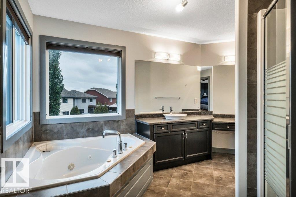 Corner soaking tub with deck-mounted fixtures, set against a large window - 1107 Chahley Crest, Edmonton, AB