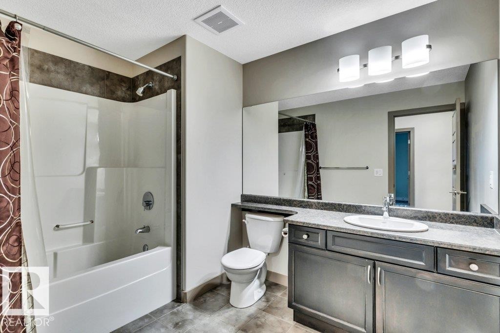 Bathroom featuring a built-in tub and shower unit, vanity with an integrated sink, dark wood-finish cabinetry, a full-width mirror, and a three-light fixture - 1107 Chahley Crest, Edmonton, AB