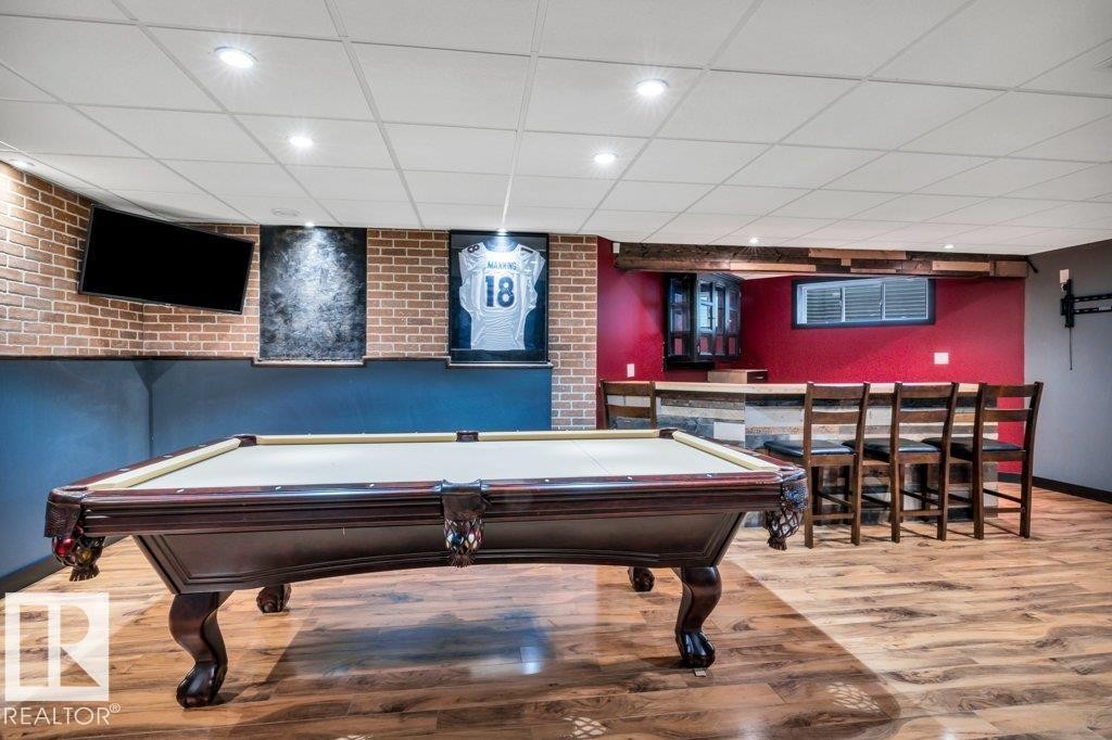Finished space featuring wood-finish flooring, a built-in bar with seating, brick-patterned wall accents, and recessed ceiling lighting - 1107 Chahley Crest, Edmonton, AB
