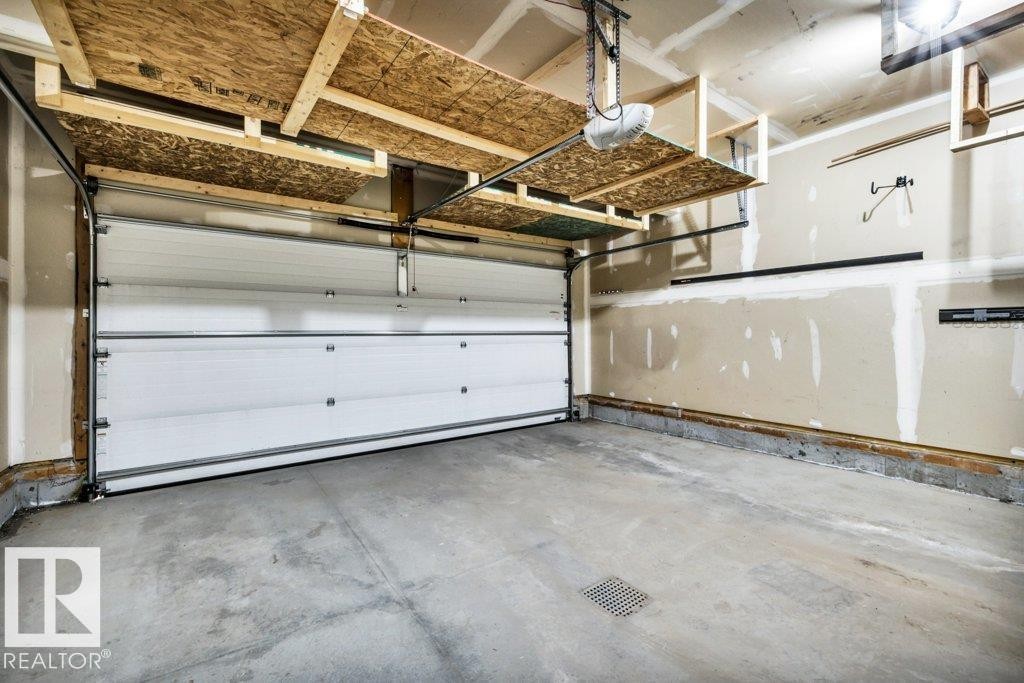 Spacious garage featuring a concrete floor, overhead shelving, automatic garage door opener, and interior wall storage systems - 1107 Chahley Crest, Edmonton, AB