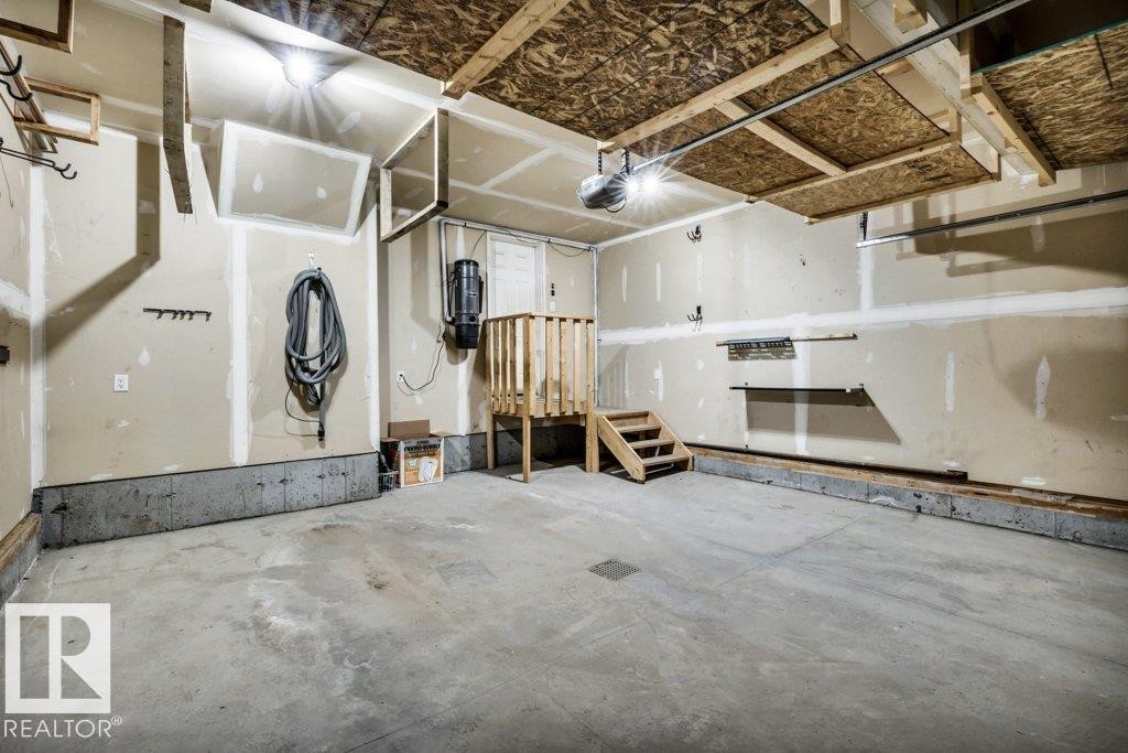 Spacious garage featuring a concrete floor, overhead storage structure, built-in shelving, and a wooden stair platform - 1107 Chahley Crest, Edmonton, AB