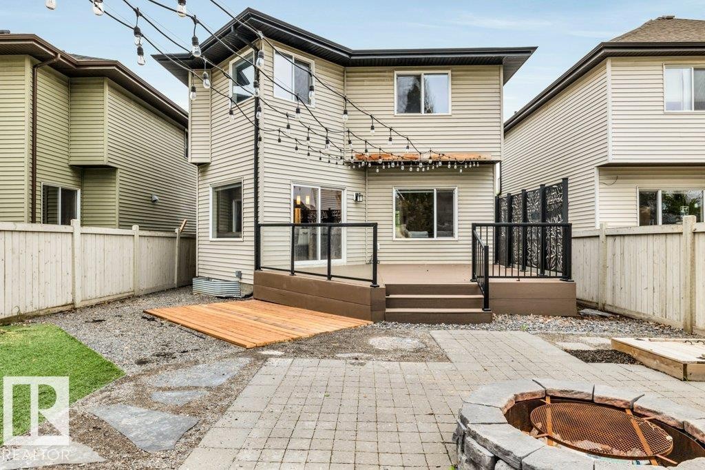 Rear exterior featuring a multi-level deck with glass panel railings, a stone-built fire pit, and string lighting - 1107 Chahley Crest, Edmonton, AB