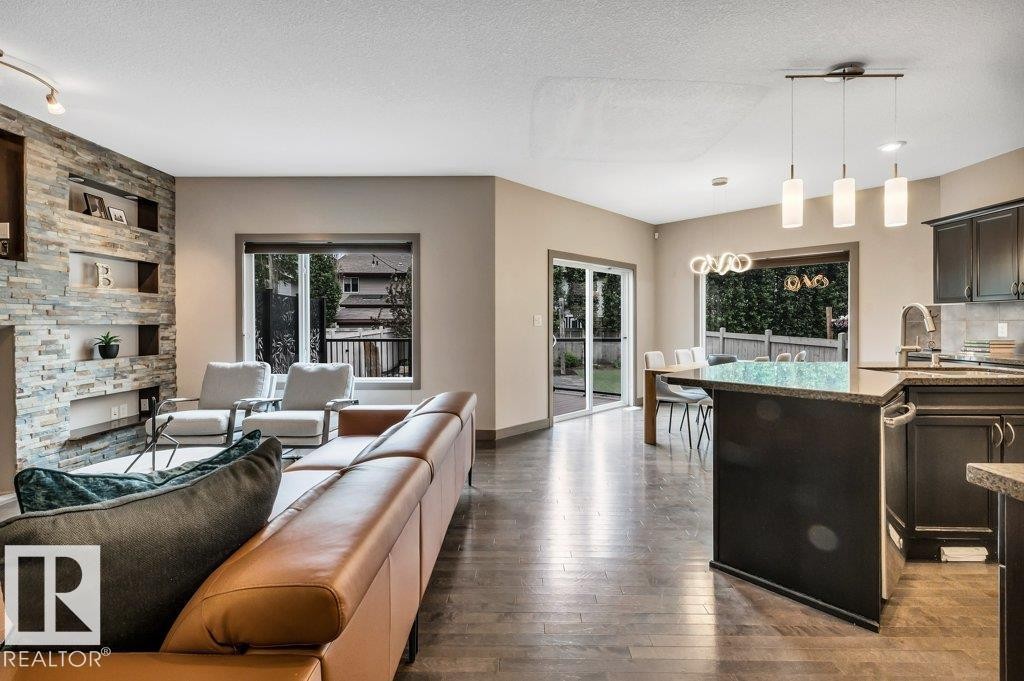 Open-concept living area featuring dark wood-finish flooring, a stacked stone accent wall with integrated shelving, and large windows - 1107 Chahley Crest, Edmonton, AB