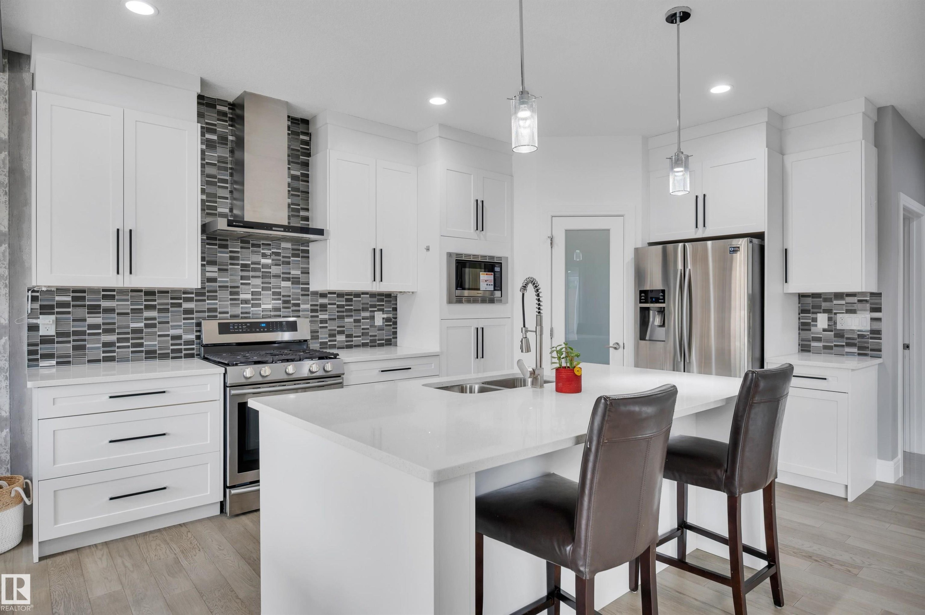 Contemporary kitchen featuring white cabinetry, stainless steel appliances, a mosaic tile backsplash, a central island with a sink, and pendant lighting - 3898 Robins Crescent Nw, Edmonton, AB - Indoor Photo Showing Kitchen With Stainless Steel Kitchen With Double Sink With Upgraded Kitchen