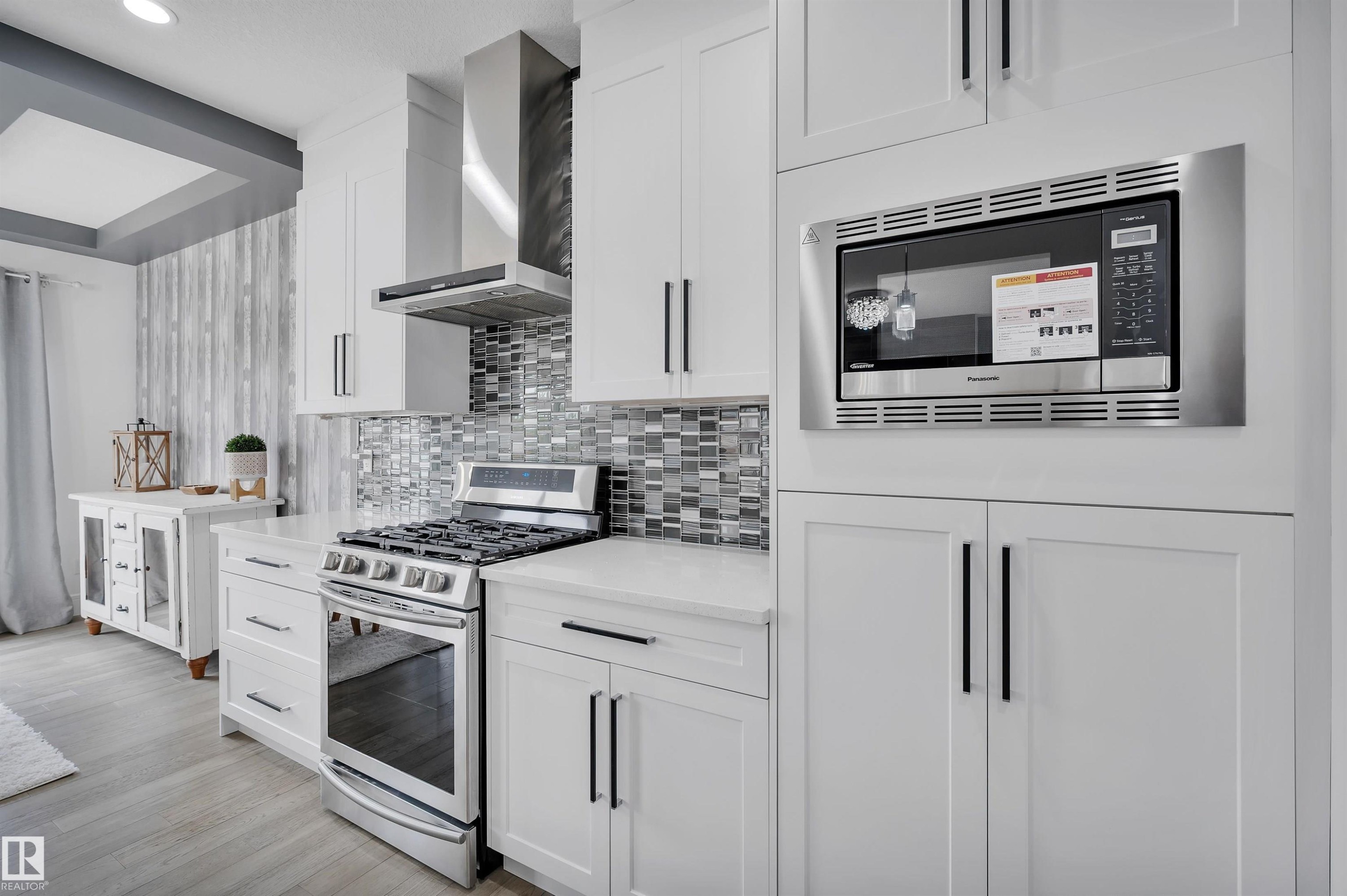 Modern kitchen featuring white cabinetry, stainless steel appliances, a mosaic tile backsplash, quartz countertops, and wood-finish flooring - 3898 Robins Crescent Nw, Edmonton, AB - Indoor Photo Showing Kitchen With Upgraded Kitchen