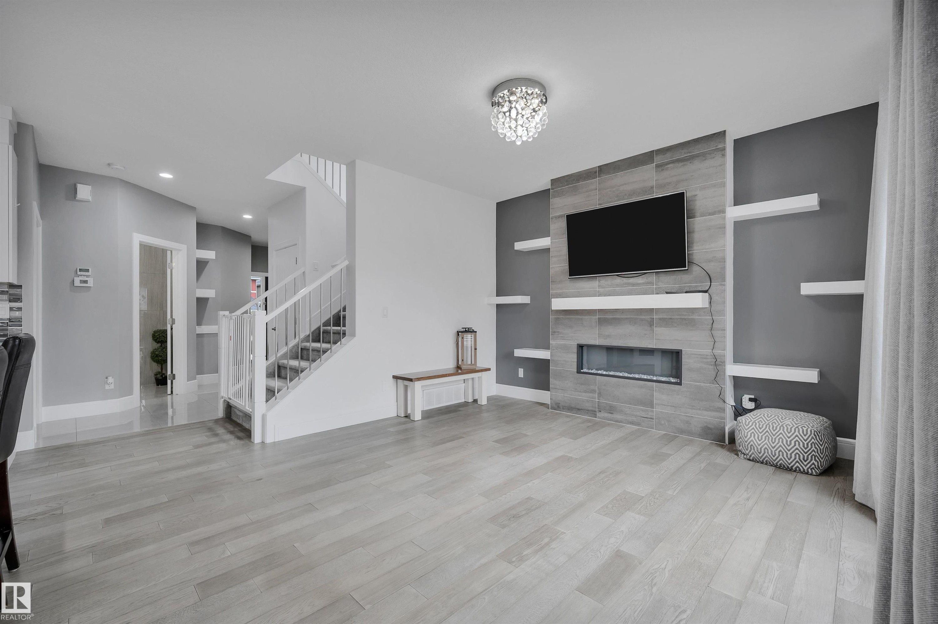 Living area featuring wood-finish flooring, a contemporary tiled fireplace surround with an integrated electric fireplace, and a crystal flush mount ceiling fixture - 3898 Robins Crescent Nw, Edmonton, AB - Indoor With Fireplace
