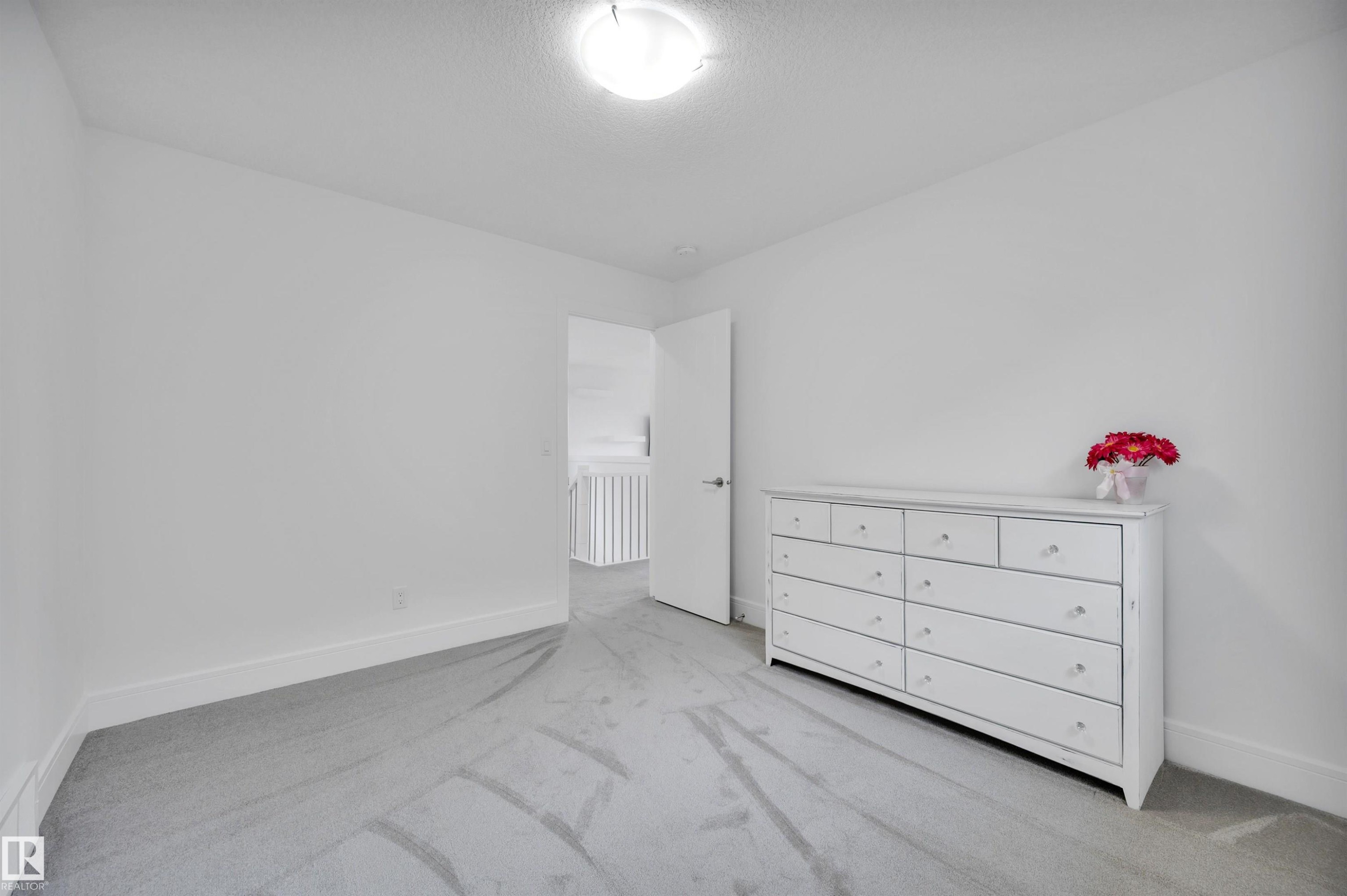 Spacious interior room featuring light gray carpeting, white baseboards, and a neutral wall palette - 3898 Robins Crescent Nw, Edmonton, AB - Indoor
