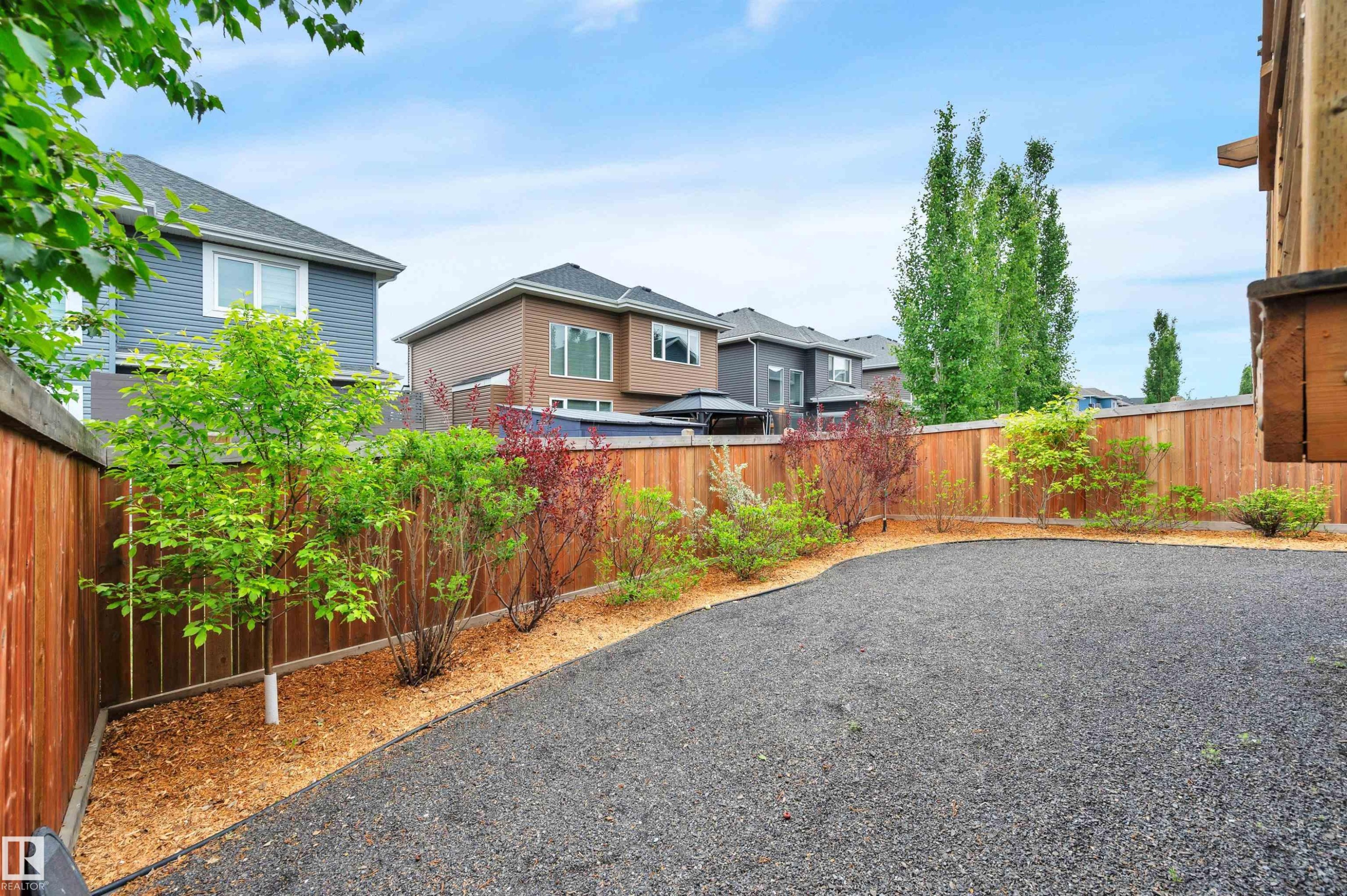 Gravel-surfaced backyard featuring new wood fencing and a landscaped perimeter with mulch and young trees - 3898 Robins Crescent Nw, Edmonton, AB - Outdoor