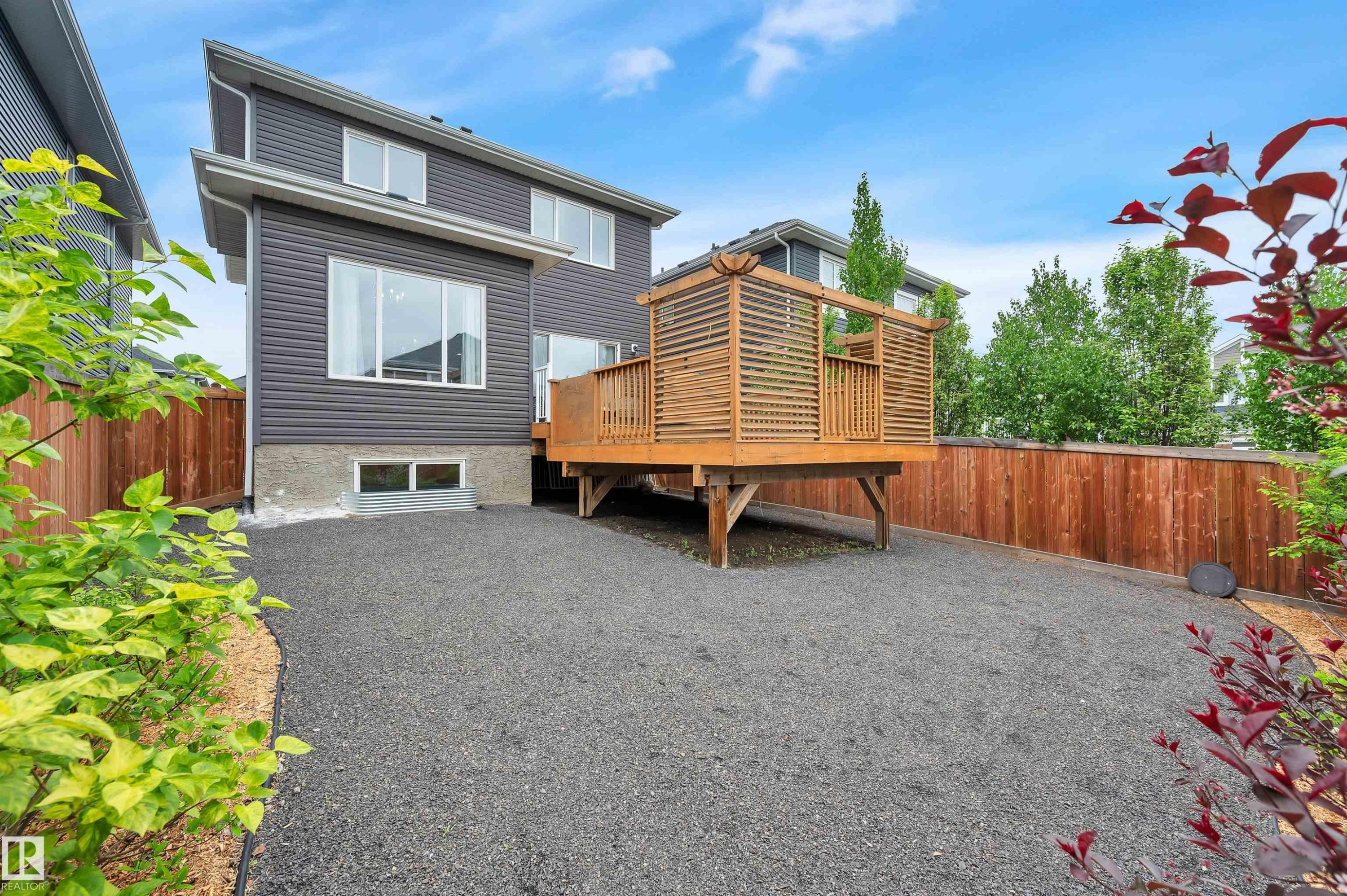 Rear exterior featuring dark gray siding, a wood deck with privacy screening, and a gravel ground cover - 3898 Robins Crescent Nw, Edmonton, AB - Outdoor