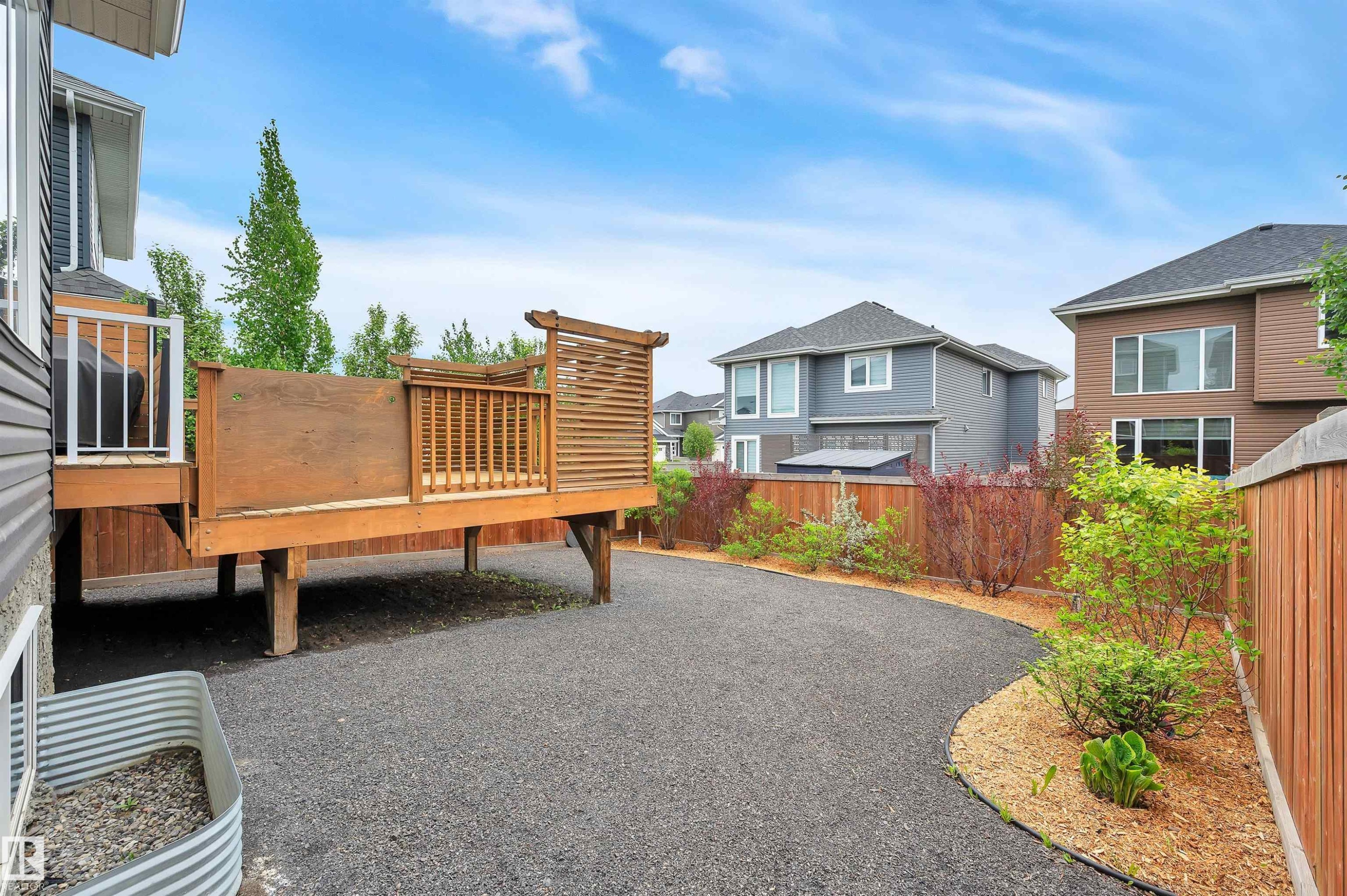 Elevated wood deck with privacy screen, gravel patio area, landscaped garden beds, and wood fencing - 3898 Robins Crescent Nw, Edmonton, AB - Outdoor With Deck Patio Veranda