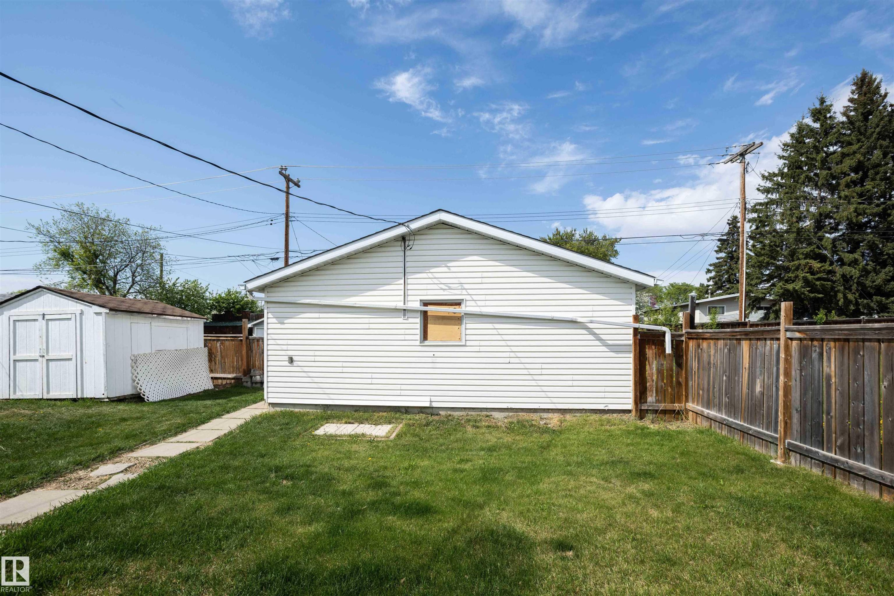 Expansive backyard with a manicured lawn, concrete pathway, white vinyl-sided structure, and a wooden privacy fence - 4414 54 Avenue, Barrhead, AB - Outdoor
