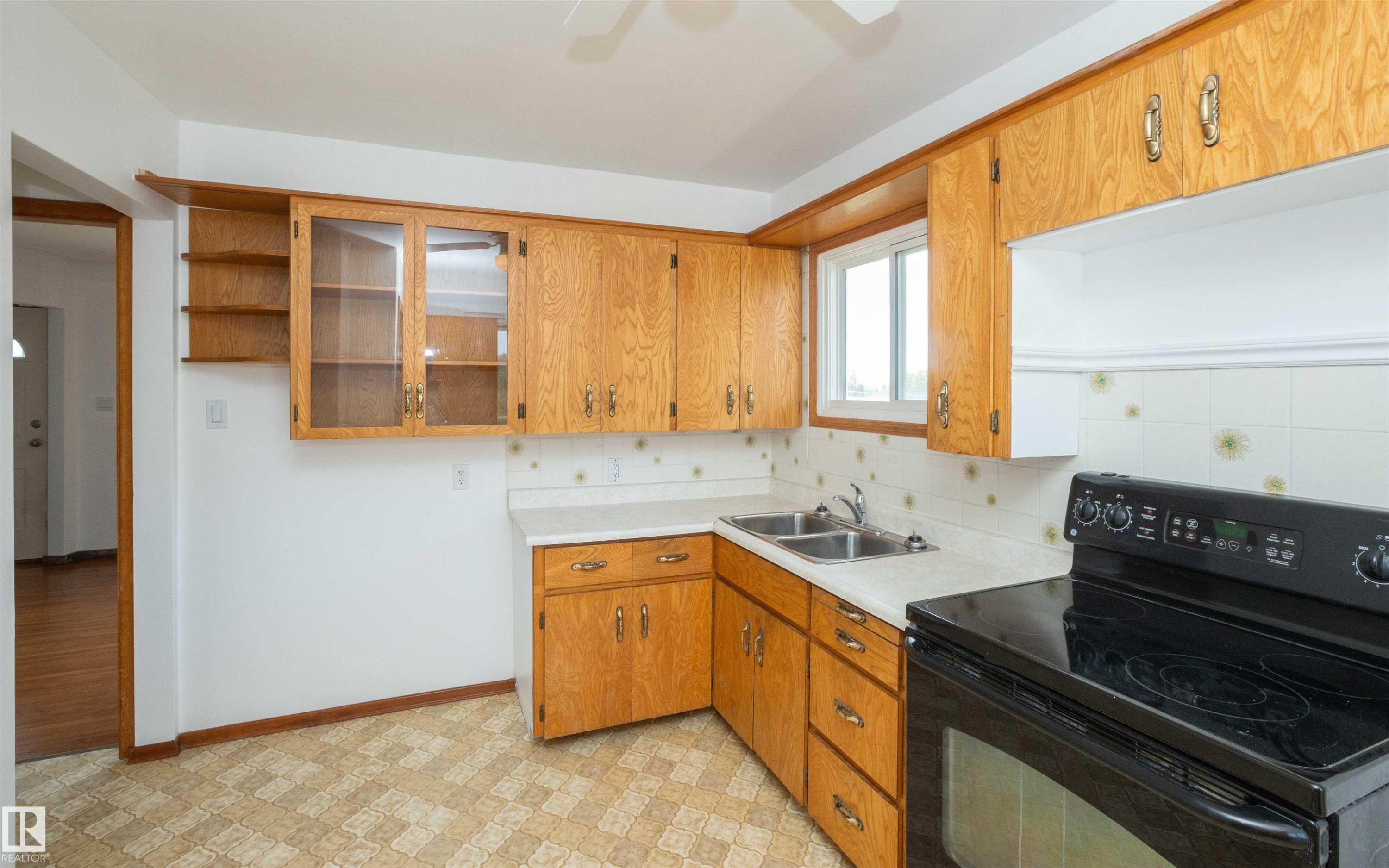 Kitchen featuring wood cabinetry, white countertops, a dual basin stainless steel sink, and a black electric range - 4414 54 Avenue, Barrhead, AB - Indoor Photo Showing Kitchen With Double Sink