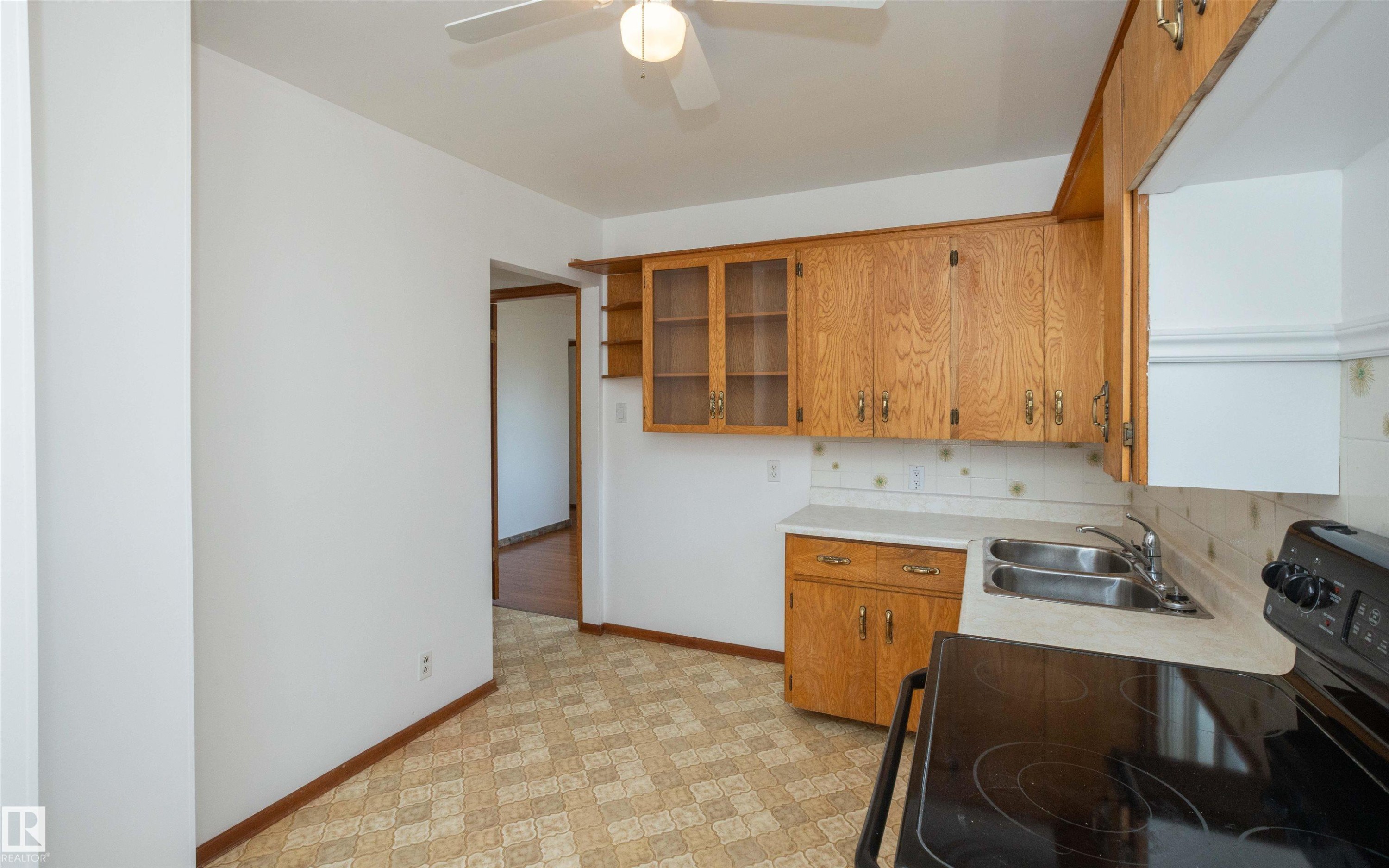 Kitchen featuring wood cabinetry, a dual-basin stainless steel sink, a black electric range, and patterned flooring - 4414 54 Avenue, Barrhead, AB - Indoor Photo Showing Kitchen With Double Sink