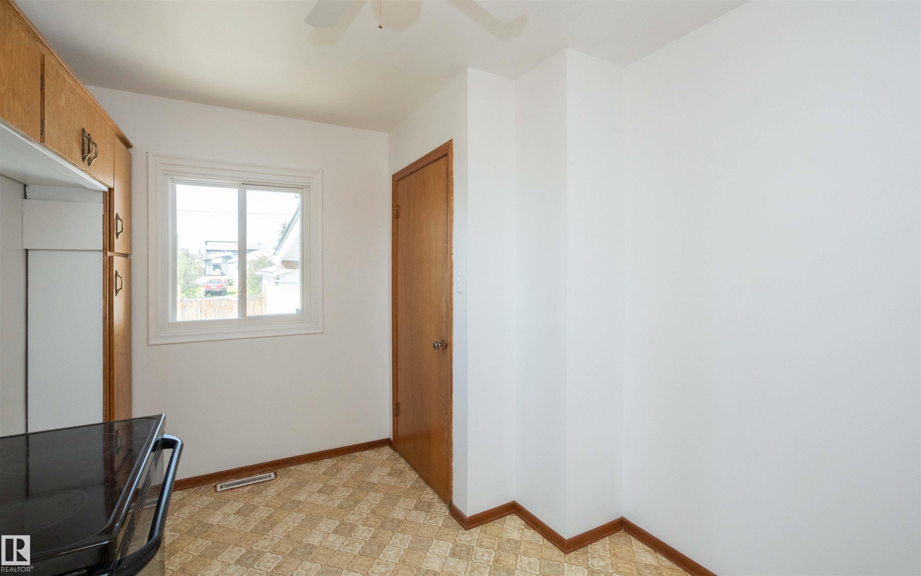 Kitchen area featuring wood-finish cabinetry, a window with white trim, and patterned floor tiling - 4414 54 Avenue, Barrhead, AB - Indoor Photo Showing Other Room