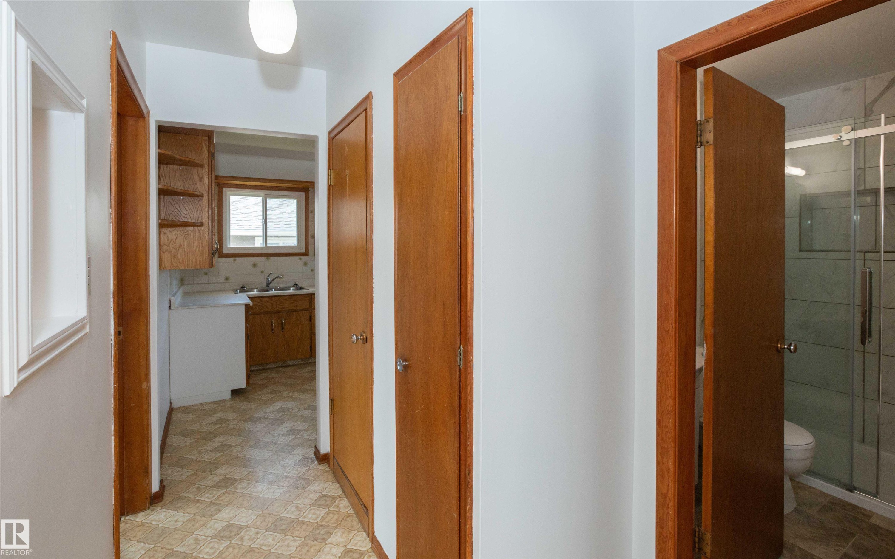 Hallway featuring wood-finish doors, a flush-mount light fixture, and patterned vinyl flooring - 4414 54 Avenue, Barrhead, AB - Indoor