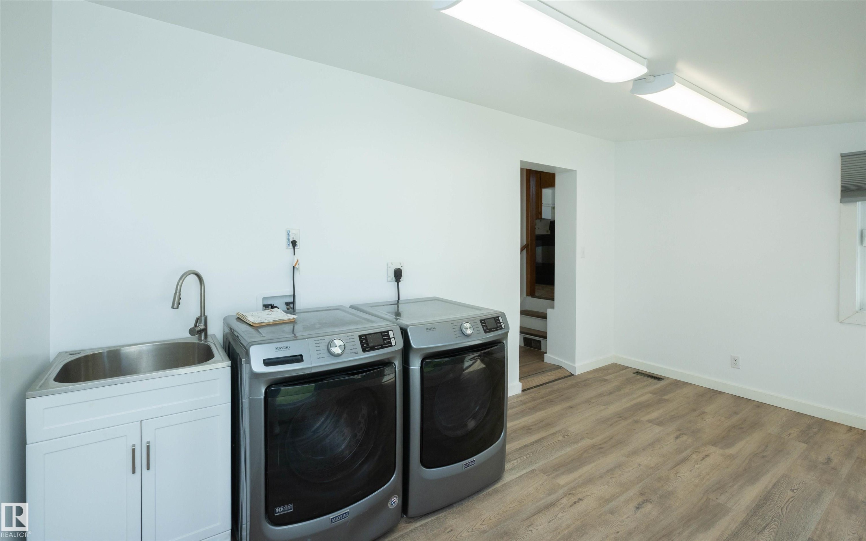 Dedicated laundry space featuring wood-finish flooring, a utility sink with white cabinetry, and overhead fluorescent lighting - 4414 54 Avenue, Barrhead, AB - Indoor Photo Showing Laundry Room