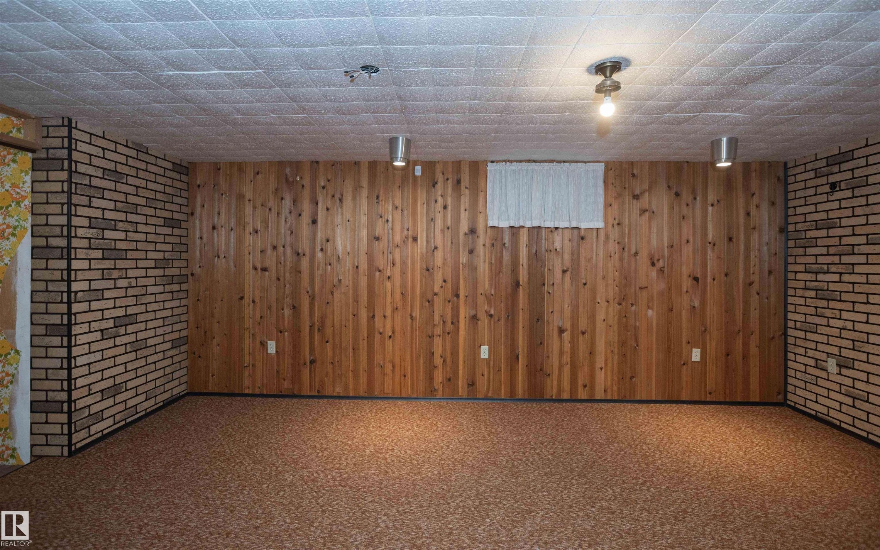Lower-level room featuring wood paneling, brick-style wall covering, and textured ceiling tiles - 4414 54 Avenue, Barrhead, AB - Indoor
