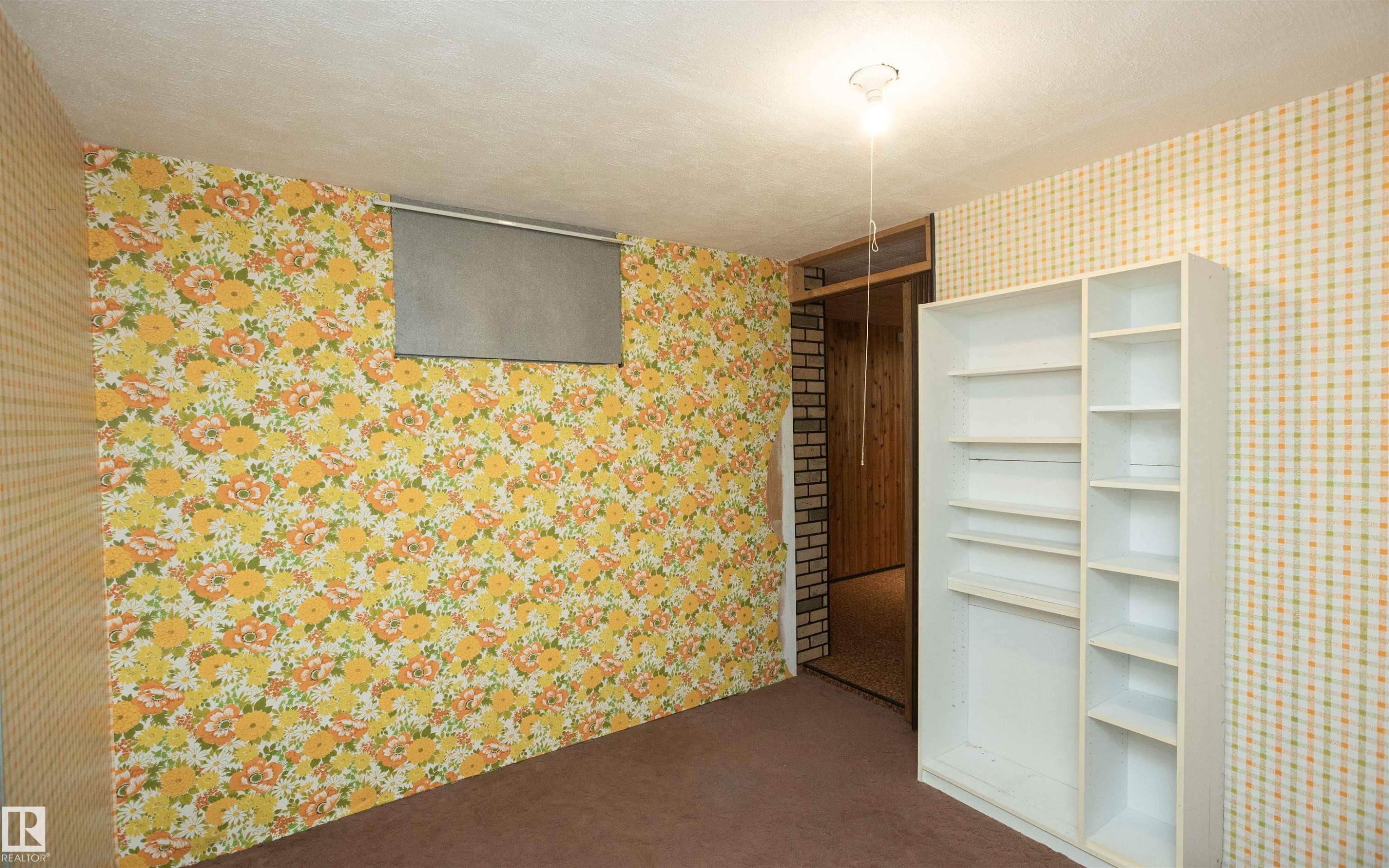 Room featuring floral and checkered wallpaper patterns, brown carpeting, and a built-in white shelving unit - 4414 54 Avenue, Barrhead, AB - With Exterior