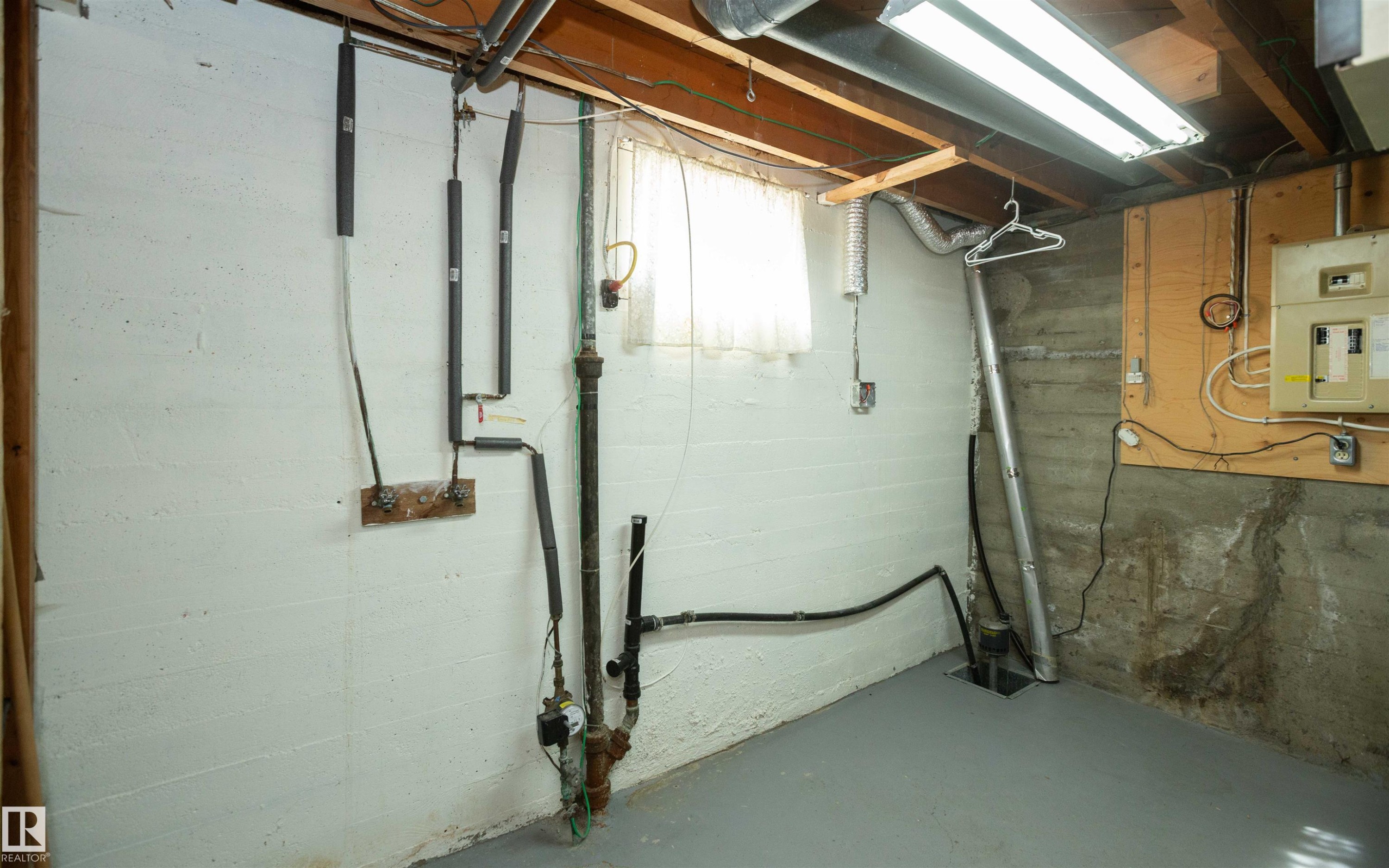 Basement utility area featuring concrete walls, exposed wood ceiling joists, overhead fluorescent lighting, and a window with white curtains - 4414 54 Avenue, Barrhead, AB - Indoor Photo Showing Basement