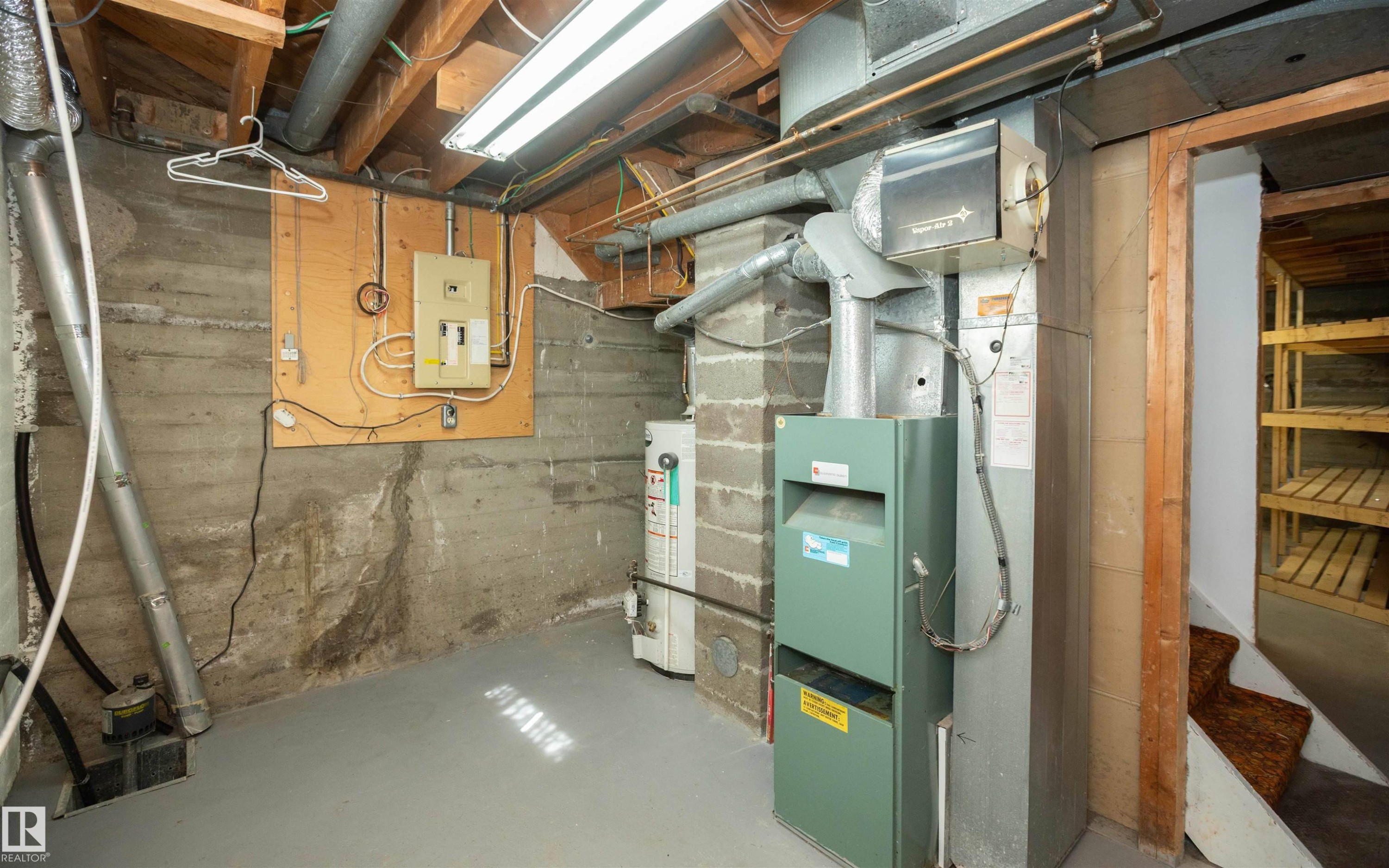 Basement utility area featuring a forced-air furnace, hot water heater, and electrical panel mounted on a wood-finish board - 4414 54 Avenue, Barrhead, AB - Indoor Photo Showing Basement