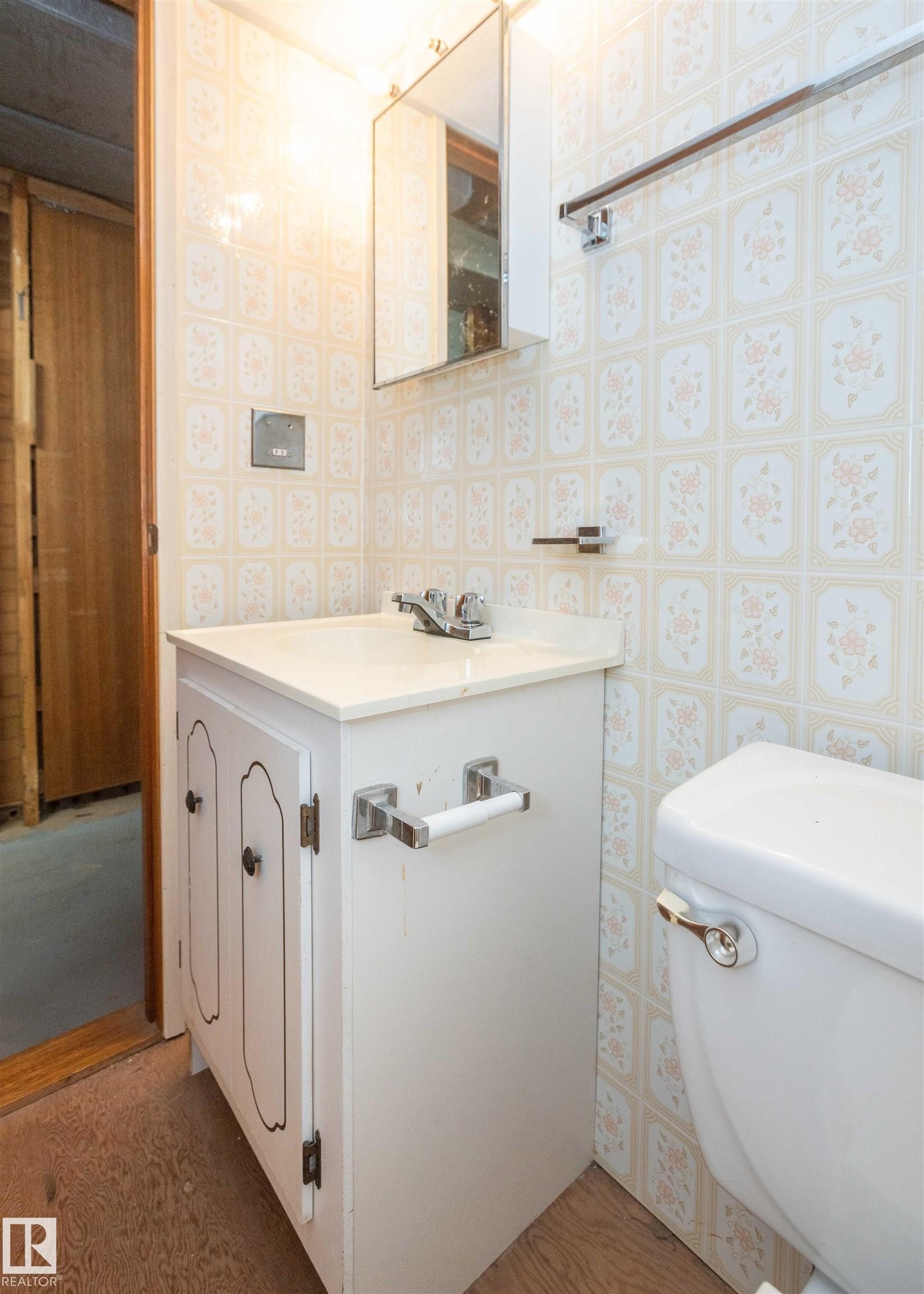 Bathroom featuring a white vanity with integrated sink, patterned wall tile, a mirrored medicine cabinet, and wood-finish flooring - 4414 54 Avenue, Barrhead, AB - Indoor Photo Showing Bathroom
