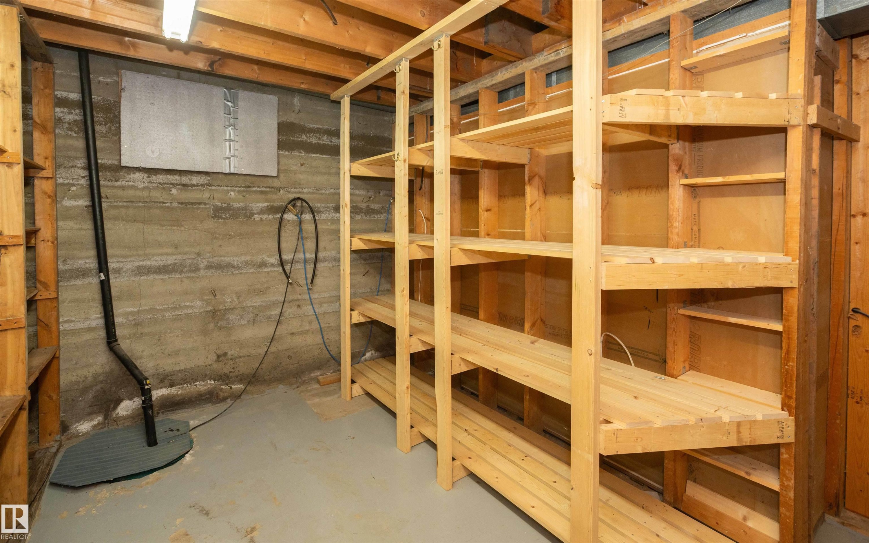 Utility space featuring extensive wood shelving, concrete walls, painted concrete flooring, and exposed ceiling joists - 4414 54 Avenue, Barrhead, AB - Indoor