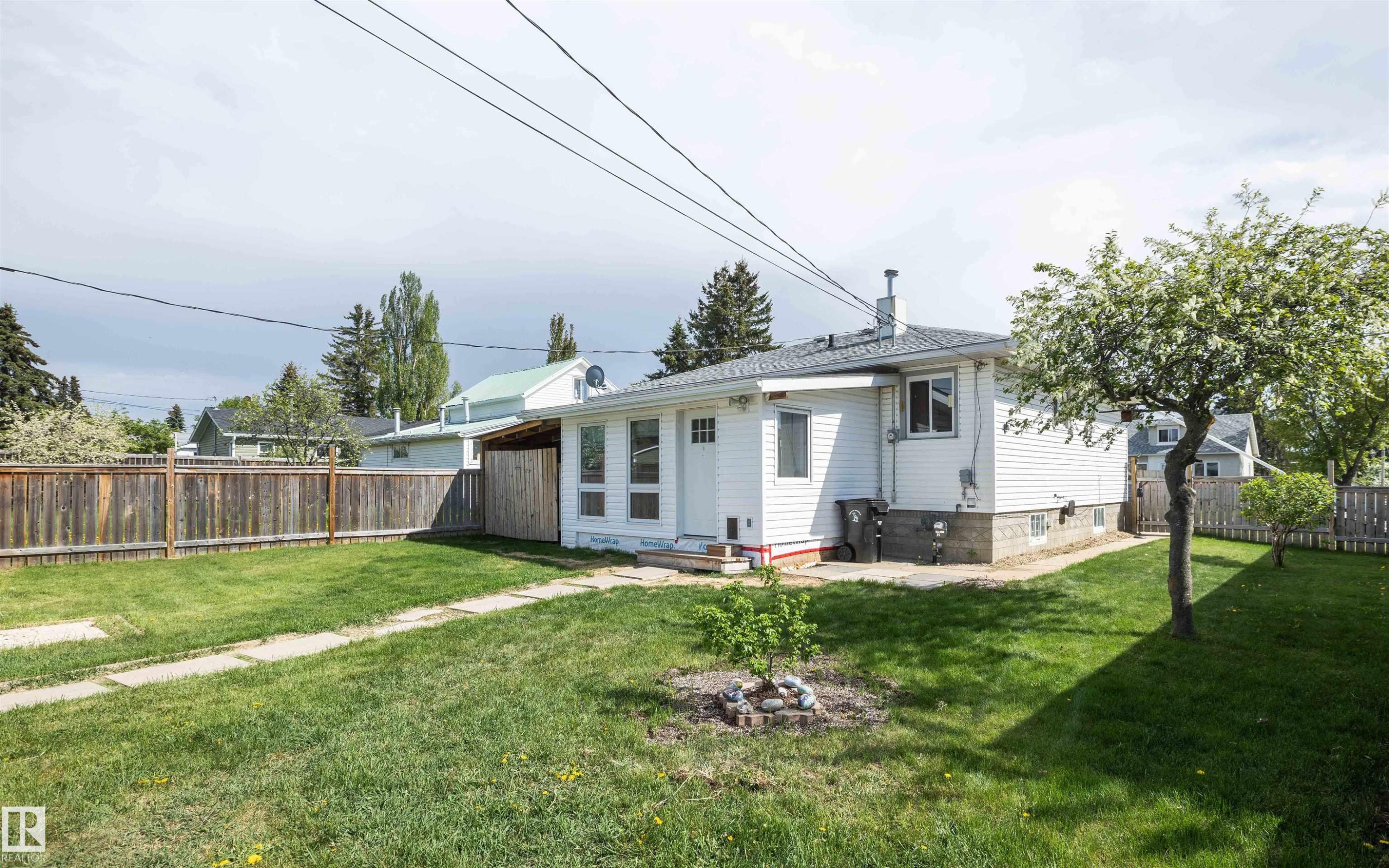 Expansive rear yard featuring mature trees, a manicured lawn, and a wood privacy fence - 4414 54 Avenue, Barrhead, AB - Outdoor