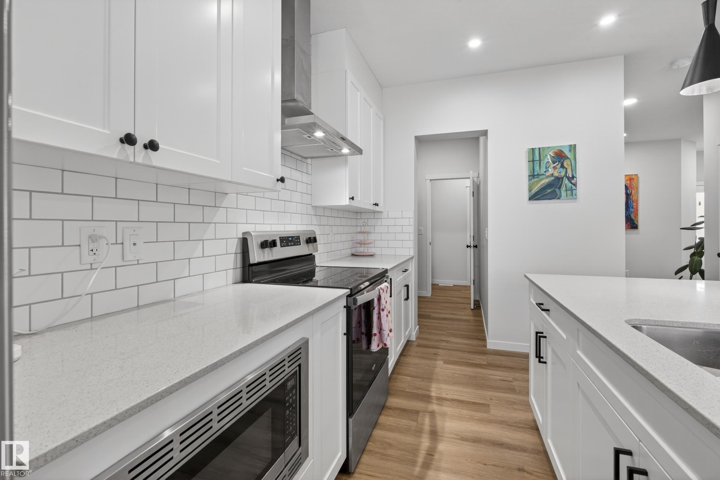 Modern kitchen featuring white shaker cabinetry, light-toned countertops, a white subway tile backsplash, and wood-finish flooring - 22836 94 Avenue, Edmonton, AB