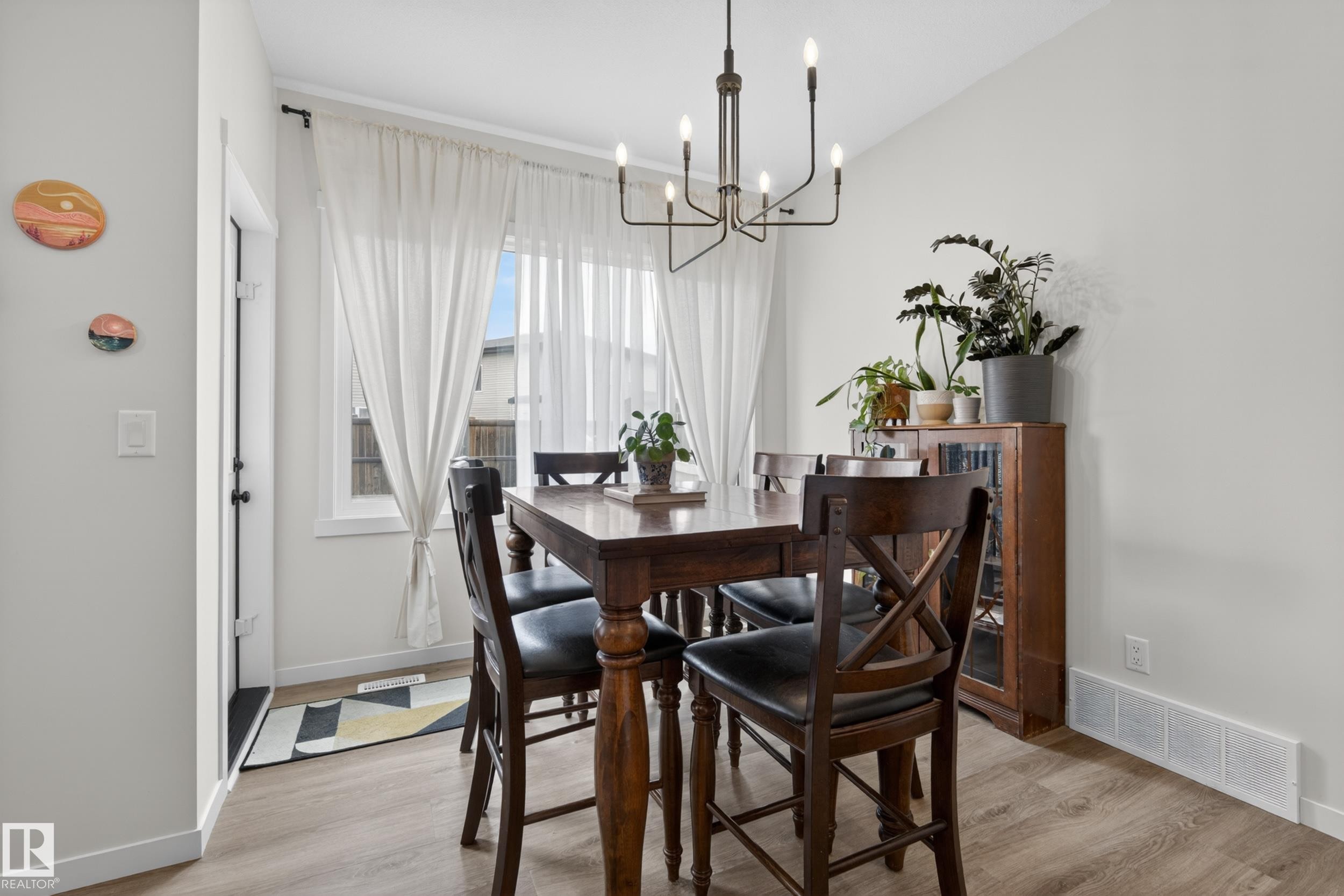 Dining area featuring wood-finish flooring, a large window with white sheer curtains, and a contemporary chandelier - 22836 94 Avenue, Edmonton, AB