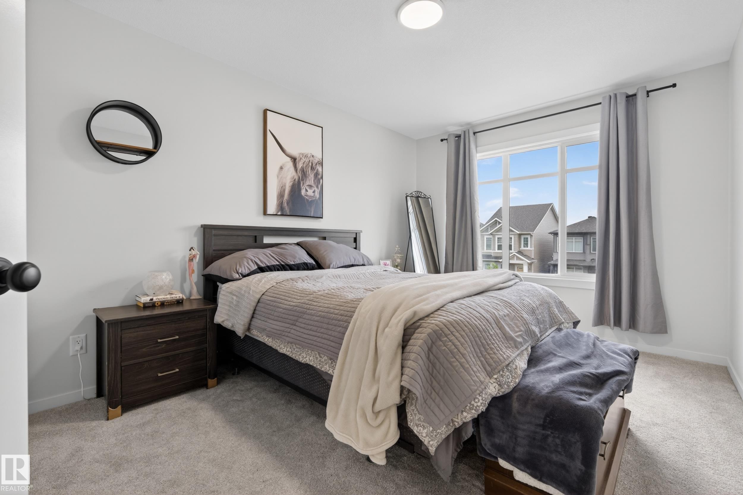 Bright bedroom featuring a large window with white framing, light gray wall paint, and gray carpeting - 22836 94 Avenue, Edmonton, AB