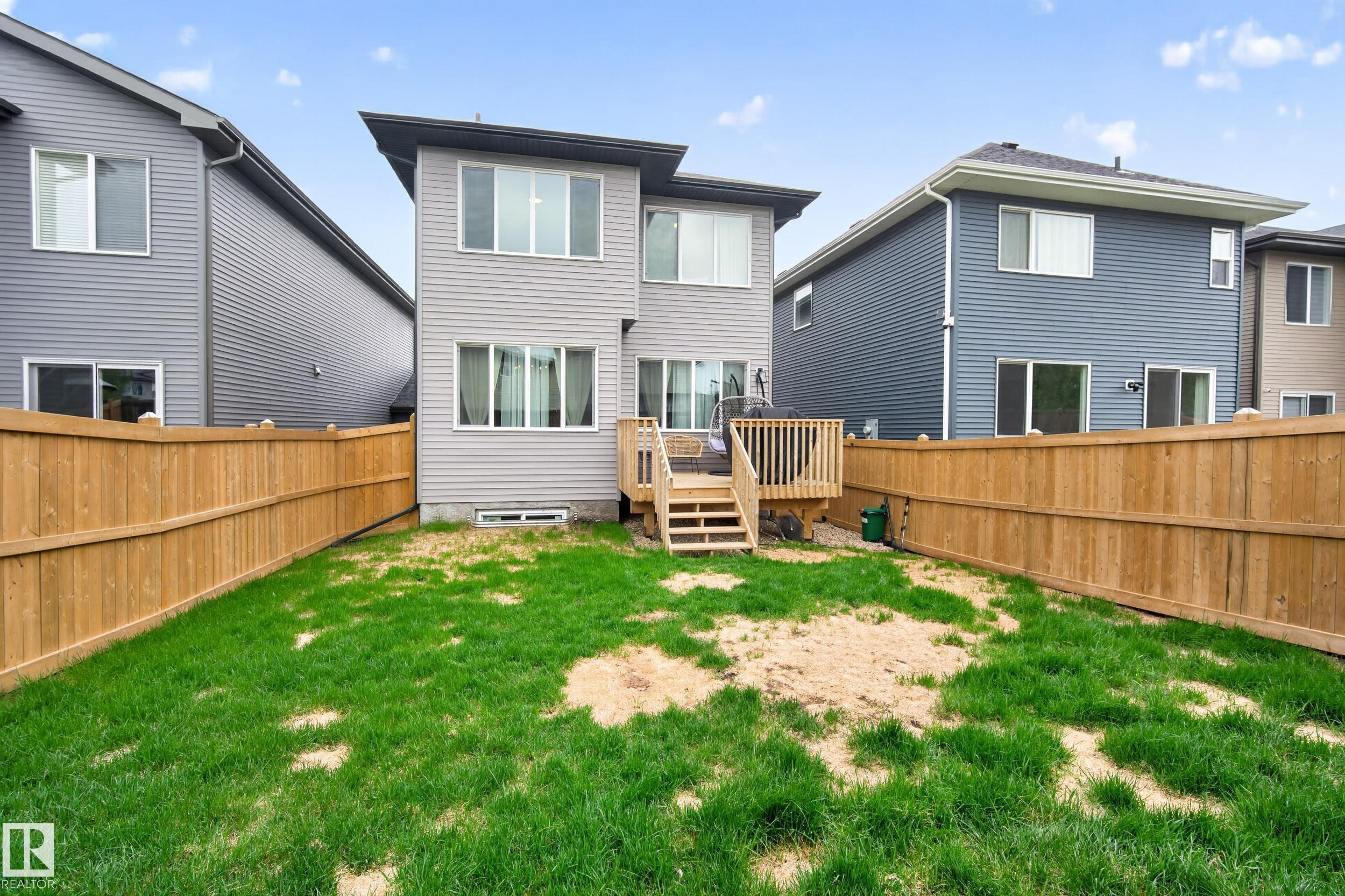 Two-story exterior featuring light gray siding, a private wood deck with stairs, a sliding glass door, multiple windows, and a full wooden privacy fence enclosing the yard - 22836 94 Avenue, Edmonton, AB