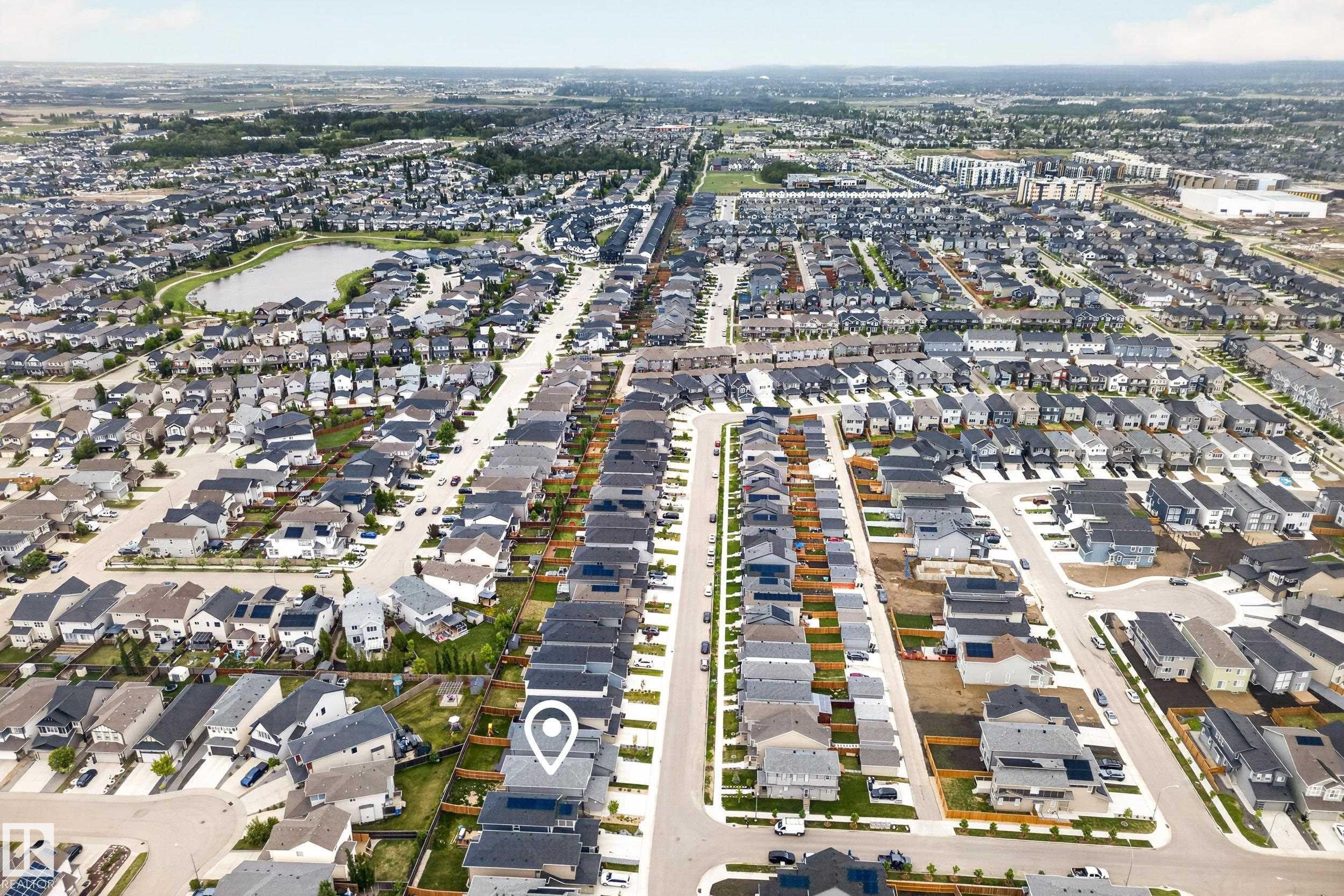 Aerial perspective showcasing a residential development with multiple detached and attached properties, featuring a central water body and extensive green spaces - 22836 94 Avenue, Edmonton, AB