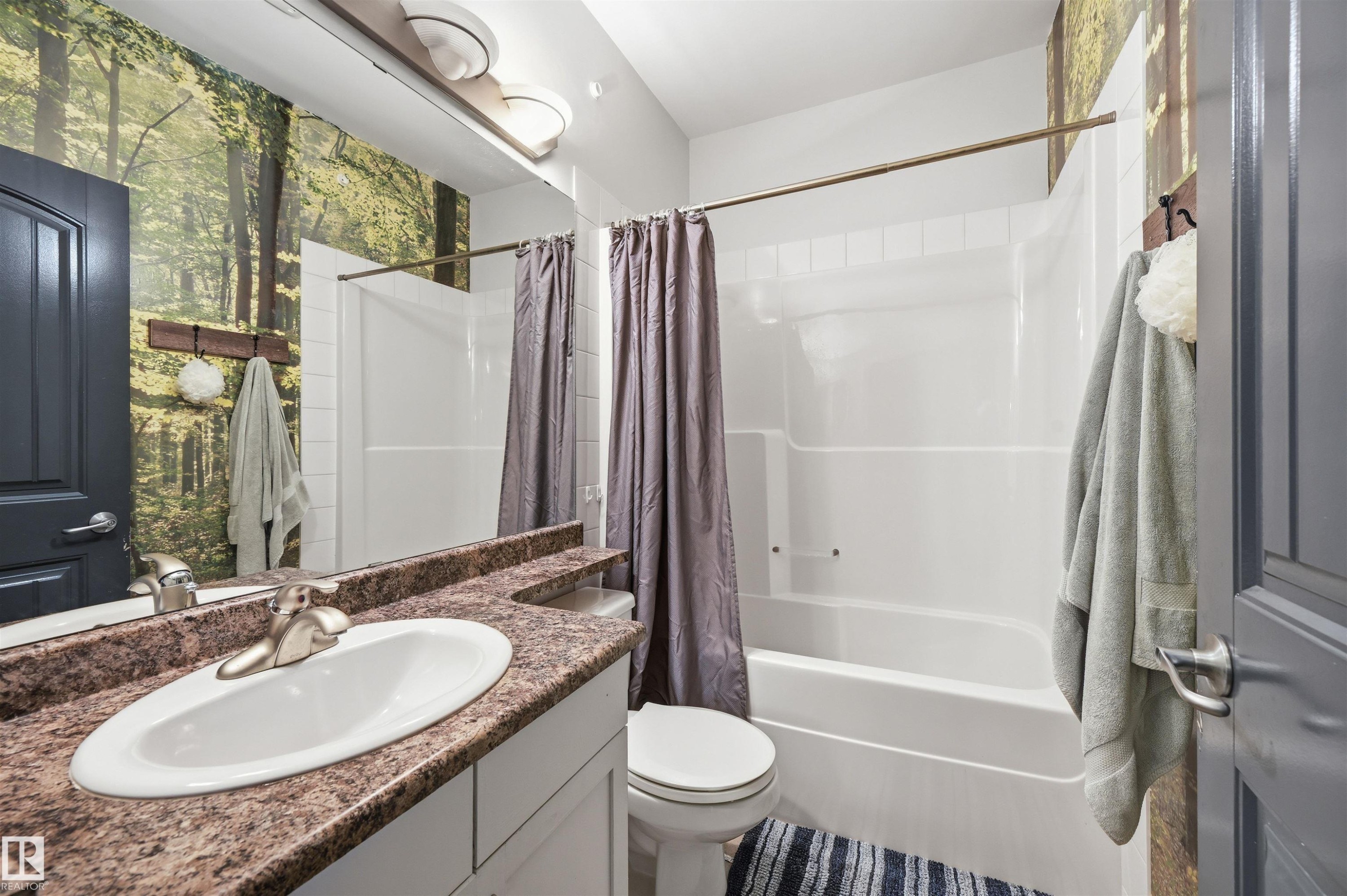 Bathroom featuring a white vanity with a drop-in sink, stone-finish countertop, and wall-mounted mirror - 217 2503 Hanna Crescent, Edmonton, AB