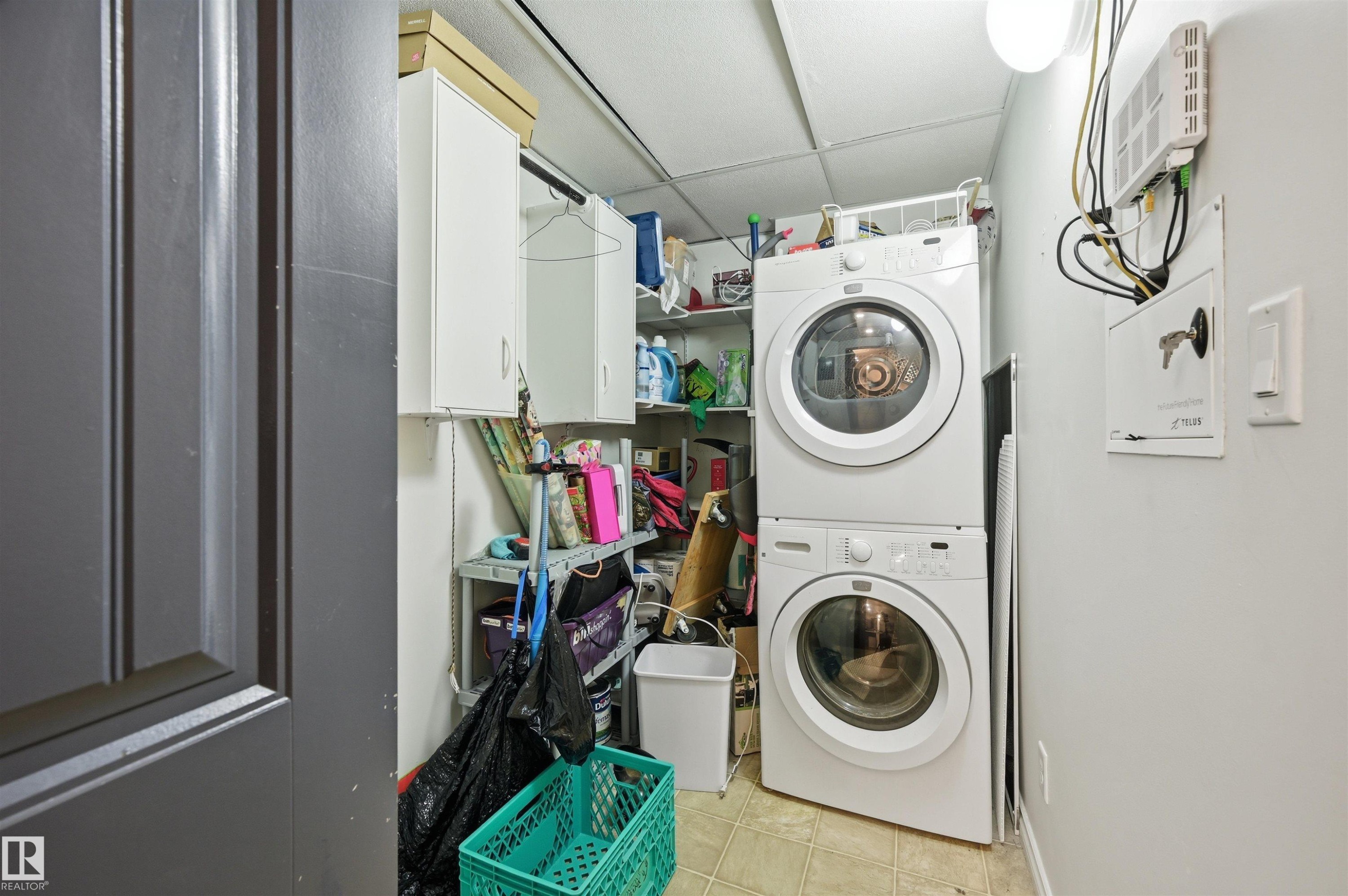 Laundry area featuring stacked front-loading appliances, overhead cabinetry, and built-in shelving - 217 2503 Hanna Crescent, Edmonton, AB